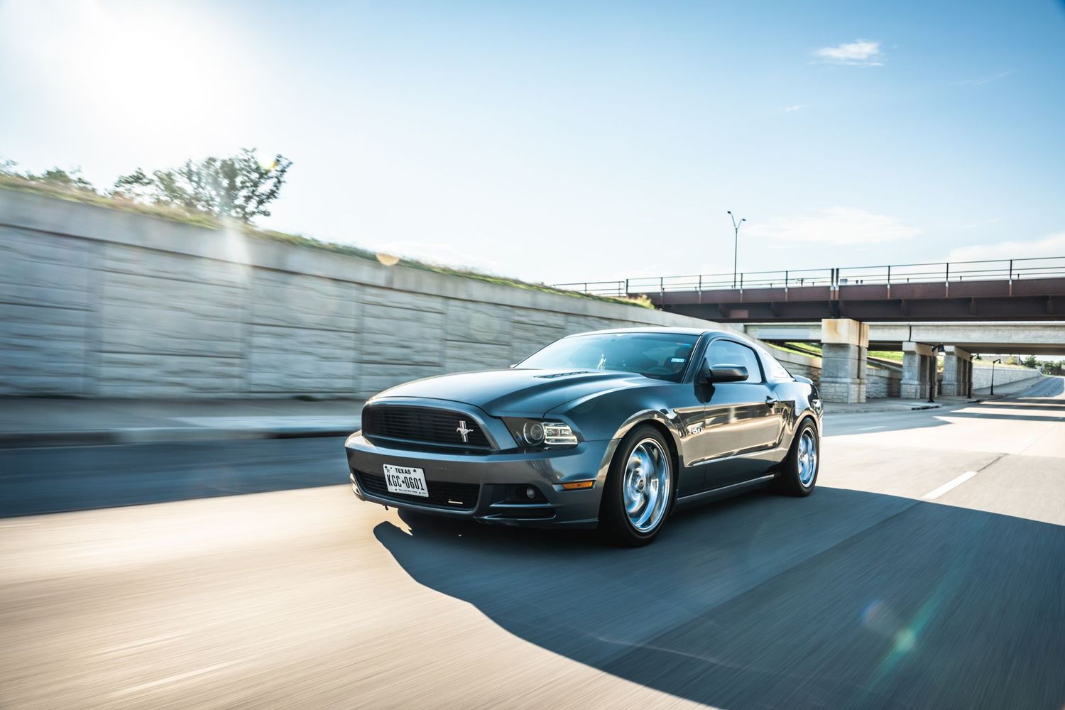 Gray Mustang photographed in motion against concrete wall and overpass background.