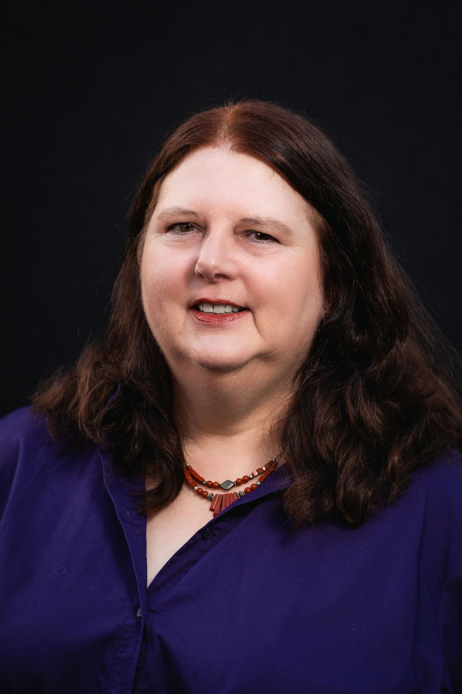 Studio portrait of woman in purple top against black background.