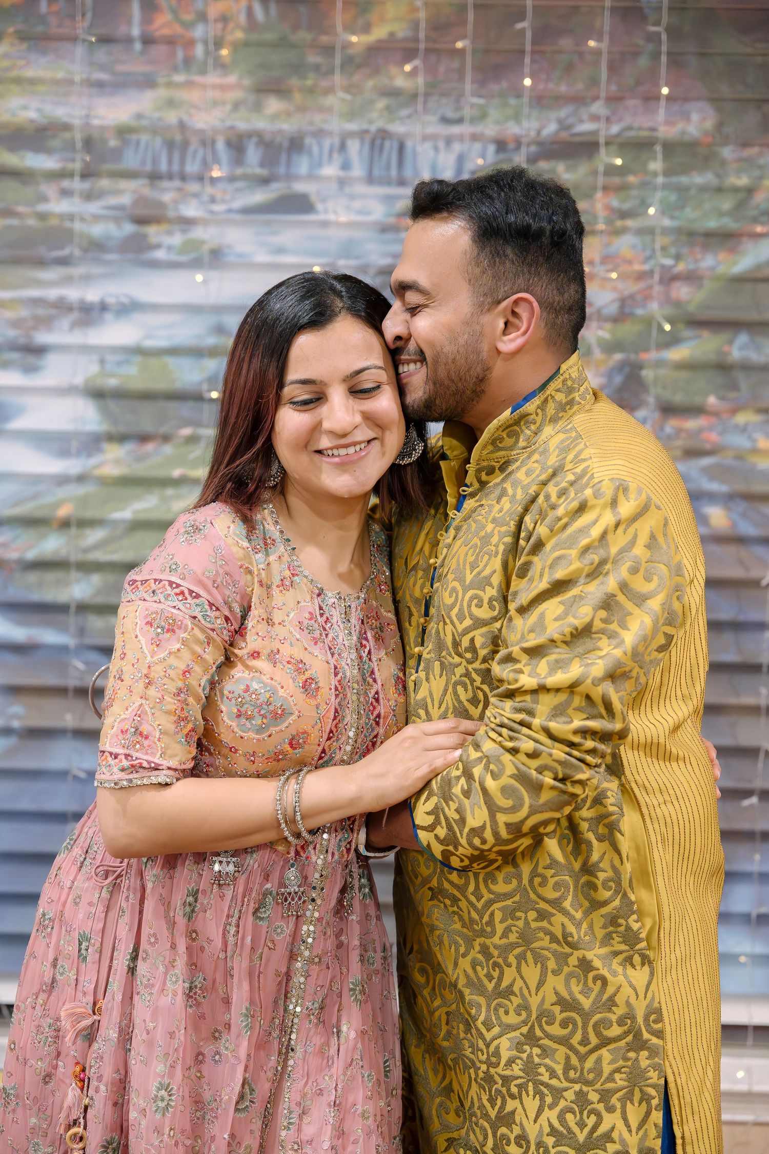 A couple in traditional Indian outfits sharing an intimate moment against fairy lights.