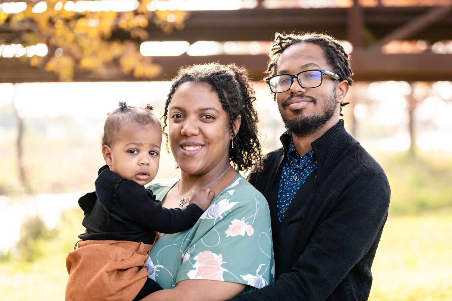 A family dressed in coordinating outfits poses together during an autumn outdoor photoshoot.