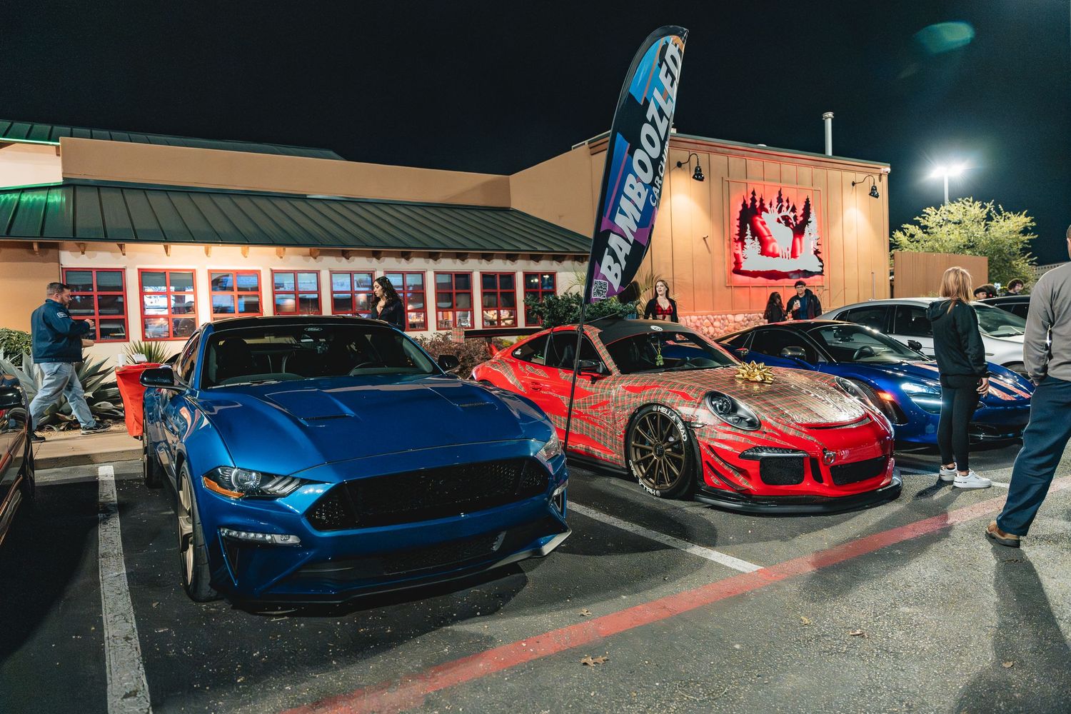 Blue Ford Mustang and red Porsche parked outside a restaurant at night.