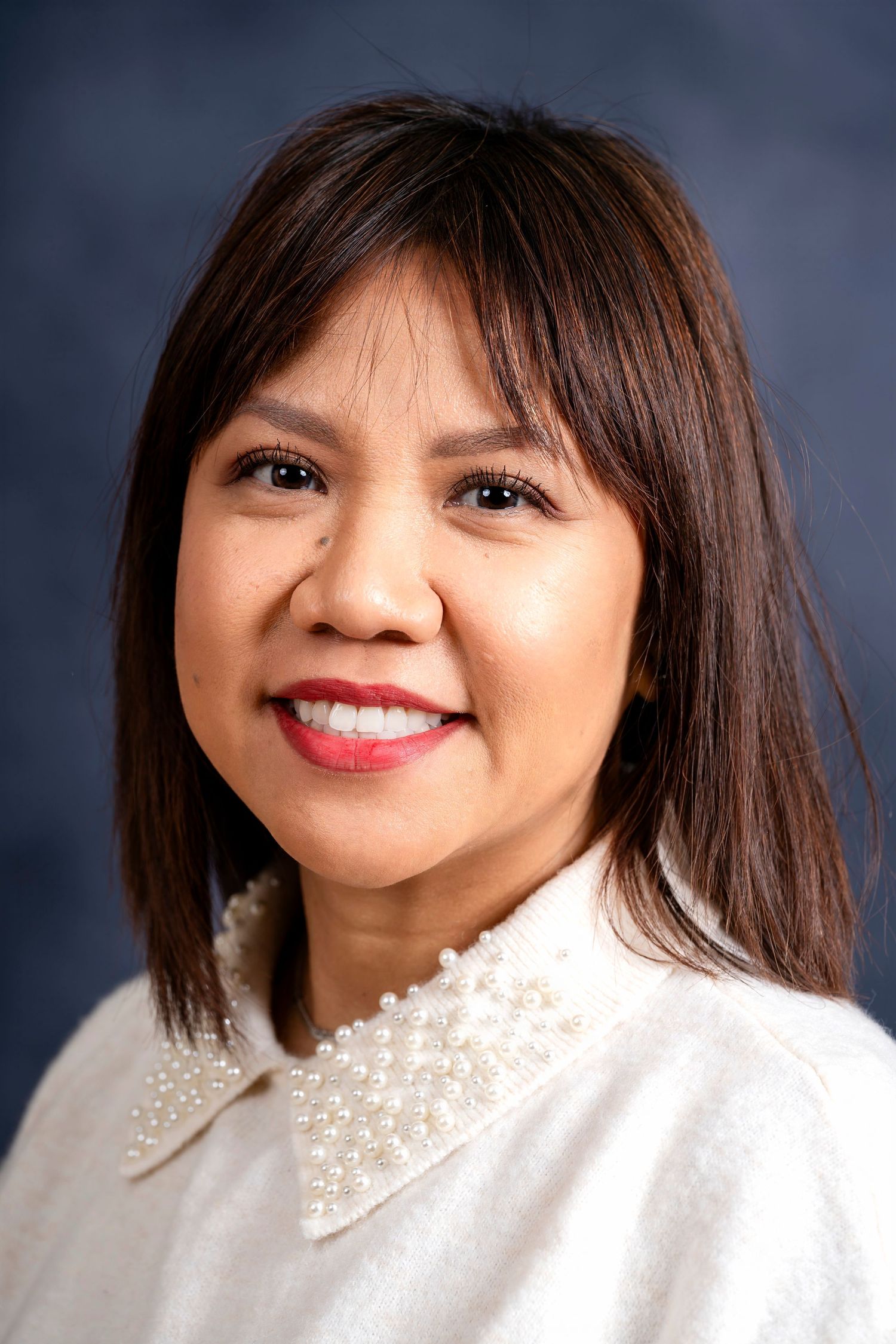 Professional headshot of woman wearing white pearl-collared sweater against dark background.