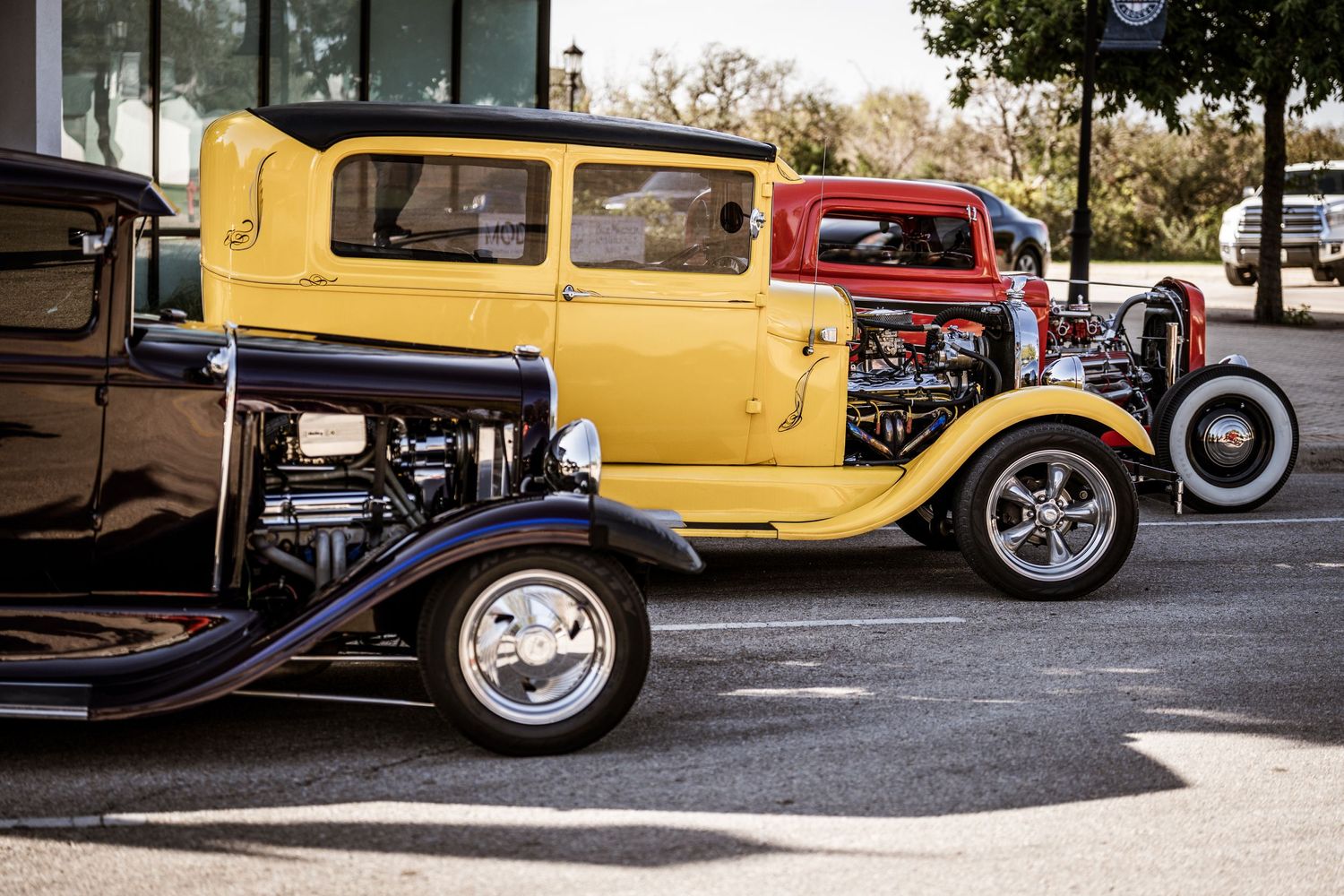 Classic yellow hot rod with custom wheels parked at a car show.