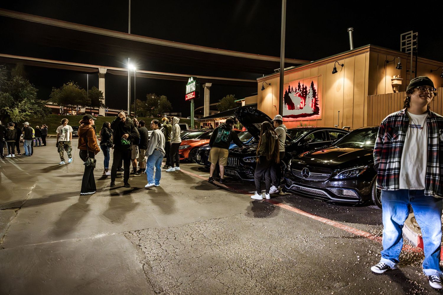 Crowd gathered at nighttime car meet with modified vehicles and lighting displays.