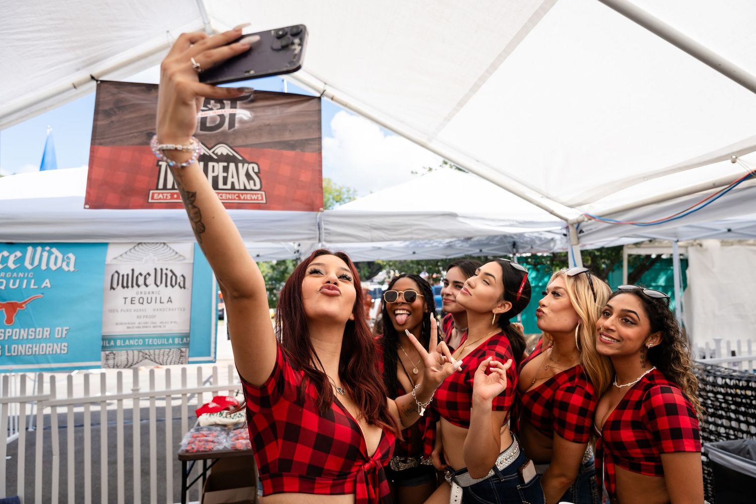 Group of people in red plaid outfits taking selfies at an outdoor event under a white tent.