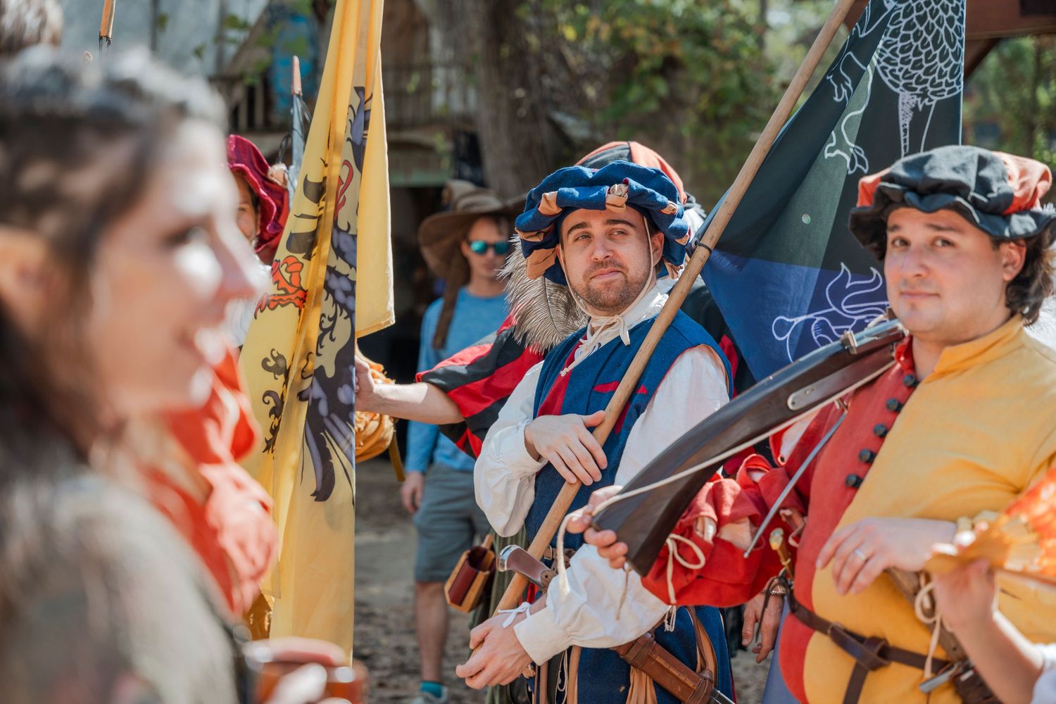 People in renaissance costumes hold flags during an outdoor festival performance.