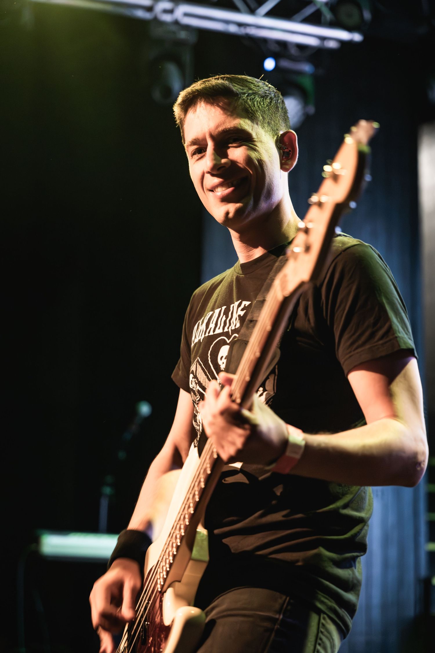 Musician plays bass guitar with joyful expression during concert performance.