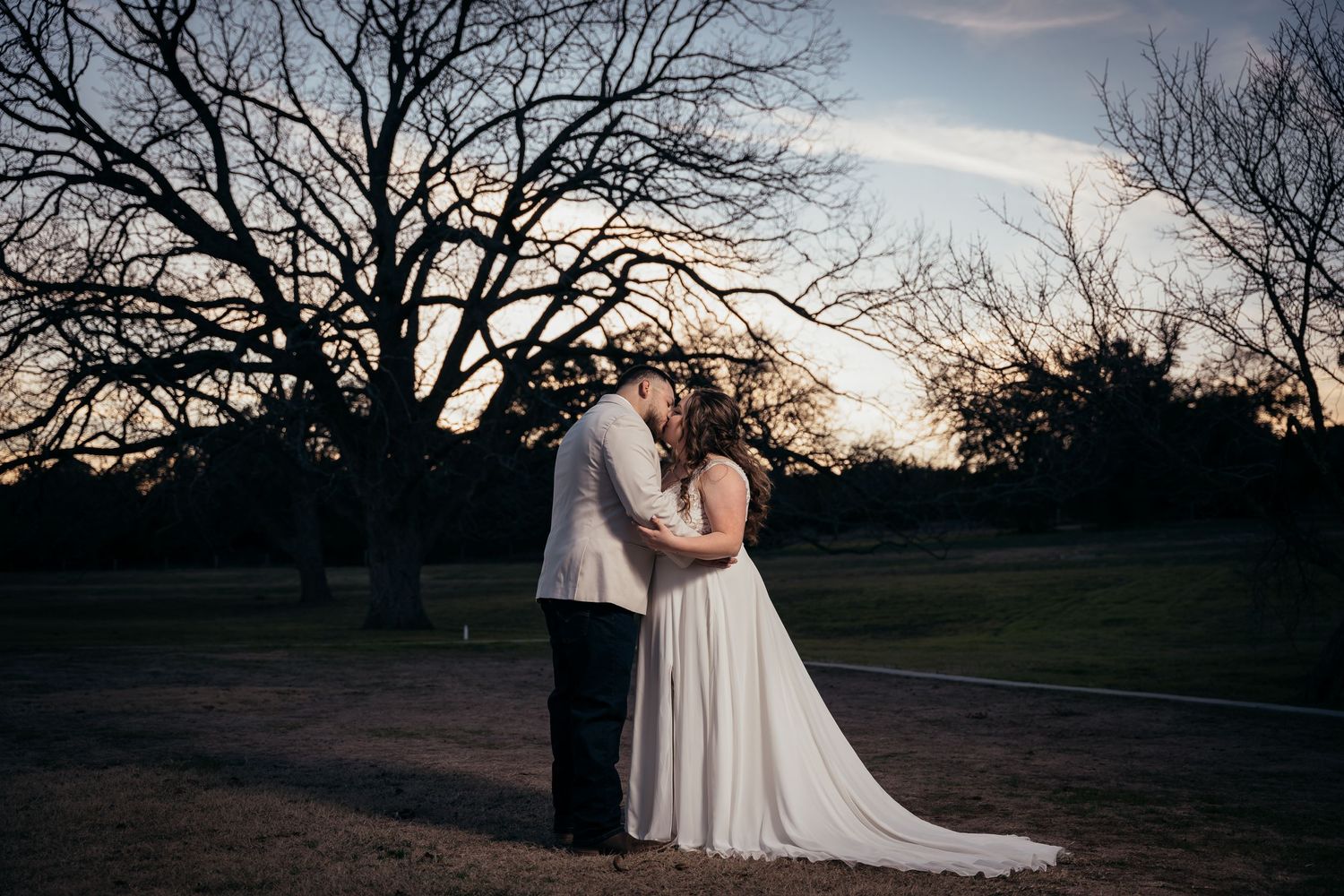 Silhouetted couple embracing at sunset with bare trees in the background.