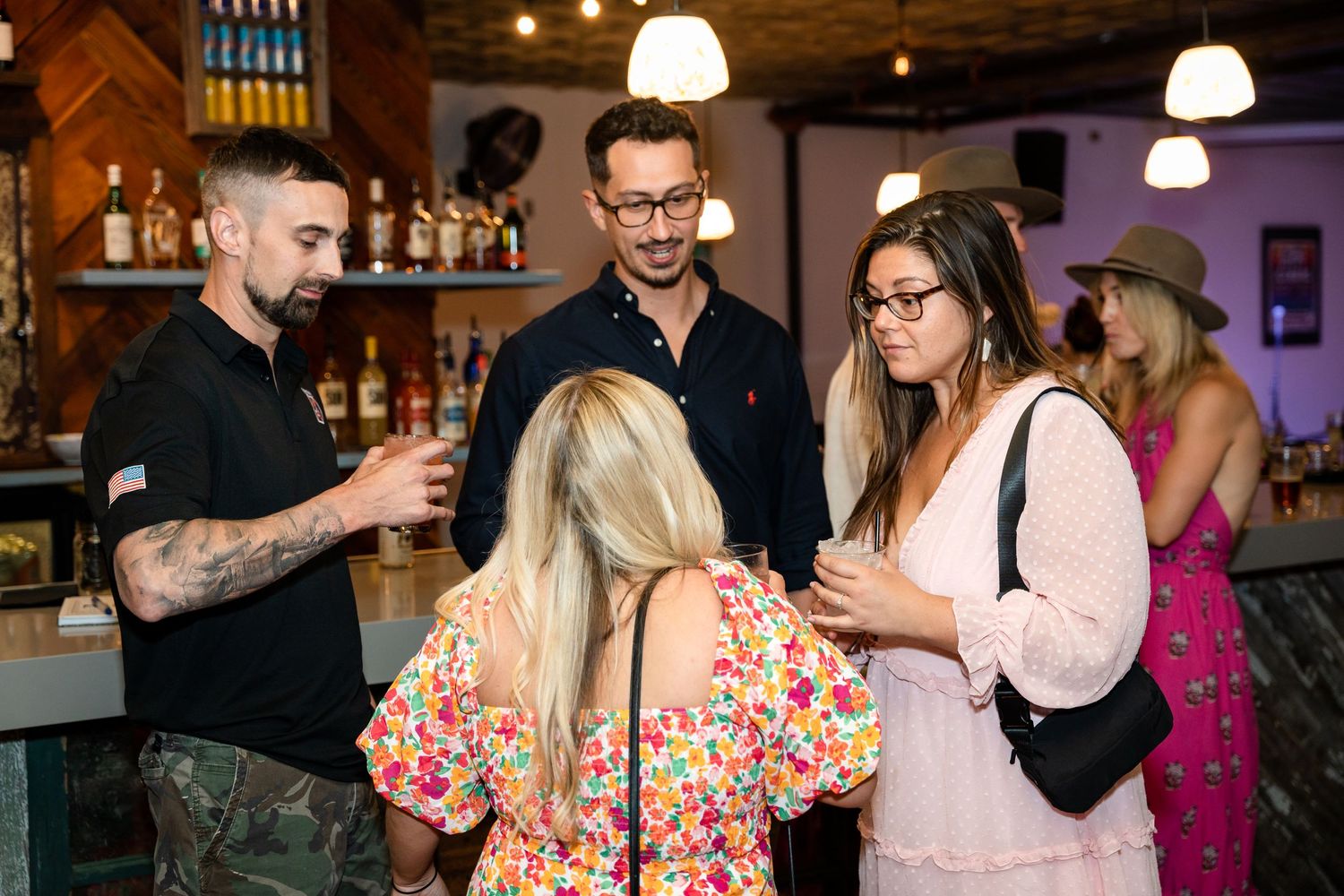Group chatting at a bar with tattoo artist and patrons in casual attire.