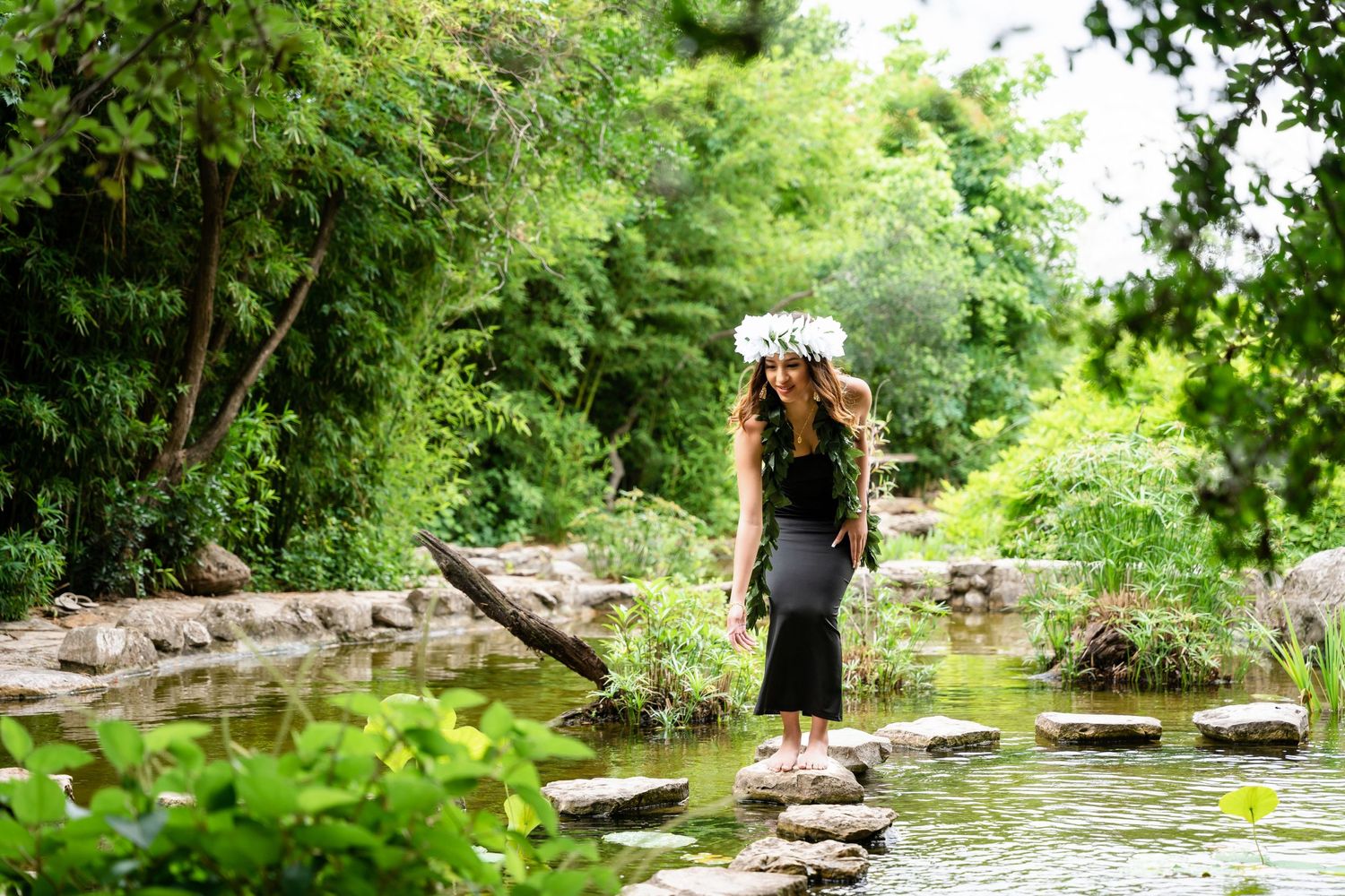 Silhouette of person in long dress standing on stones beside garden pond.