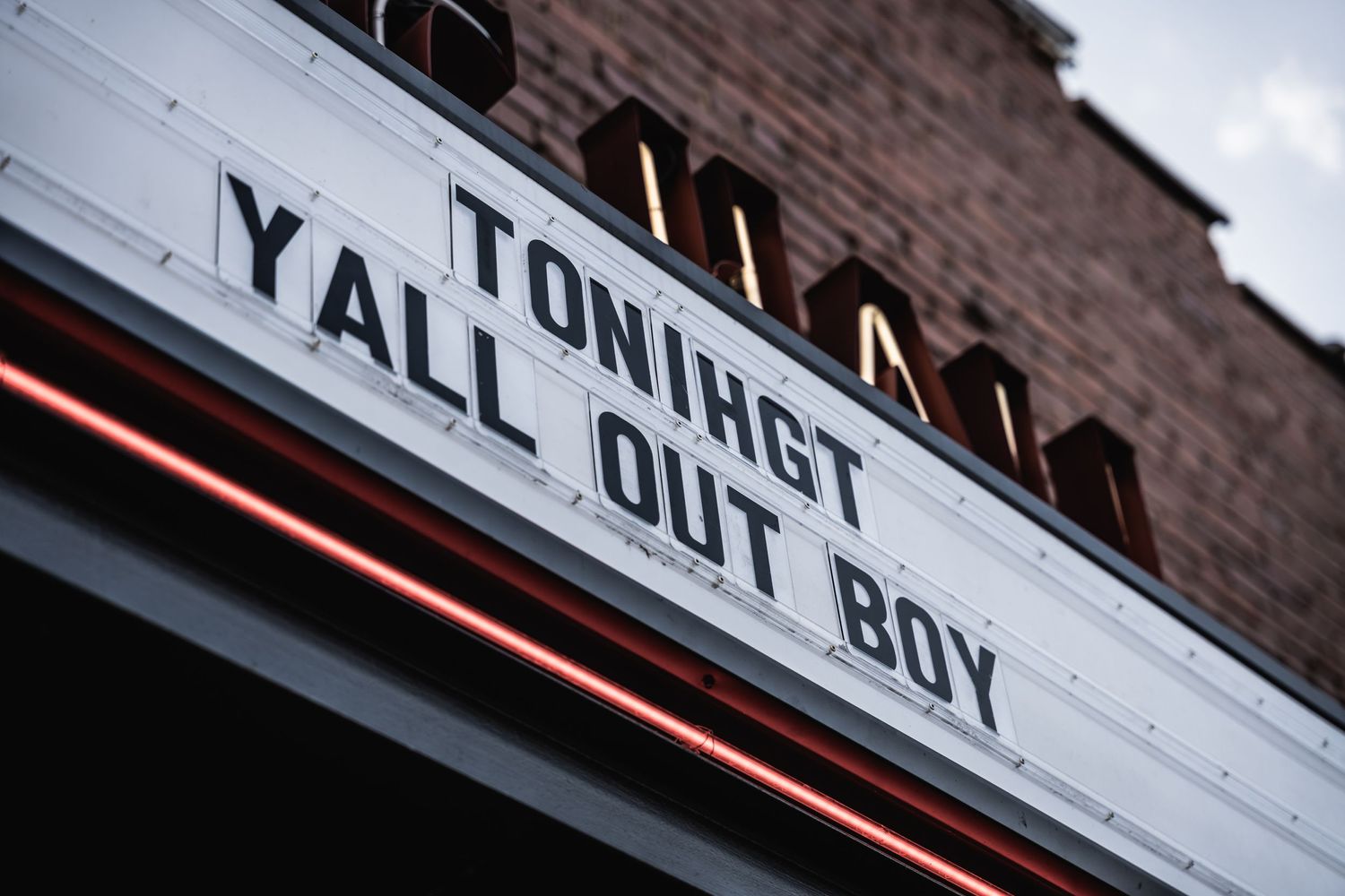 White marquee lettering on dark background reading 'Tonight Yall Out Boy' with moody evening lighting.