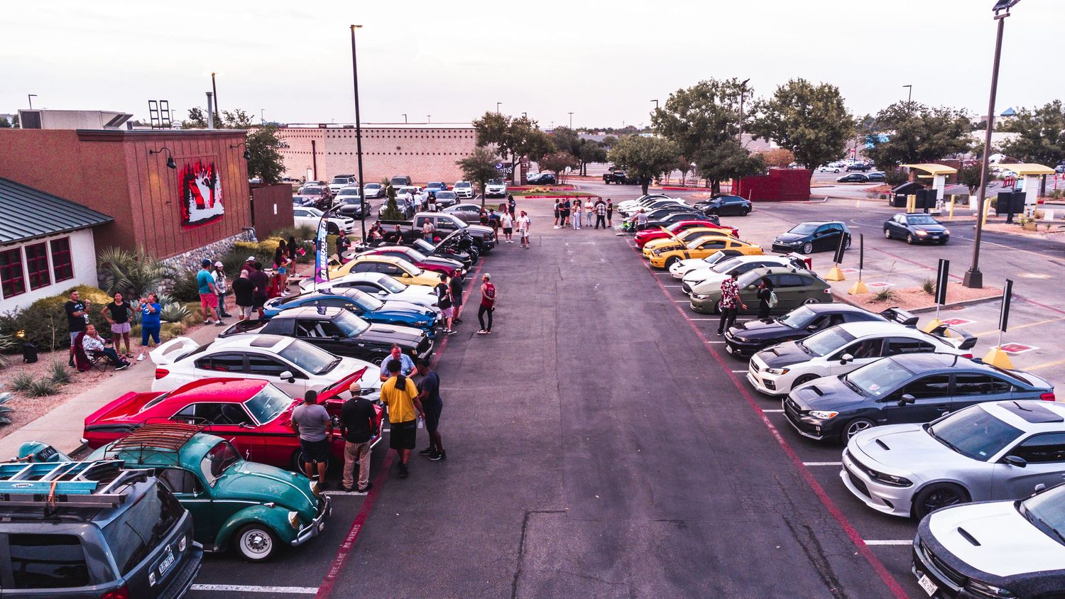 Bird's eye view of crowded car show in commercial parking lot.