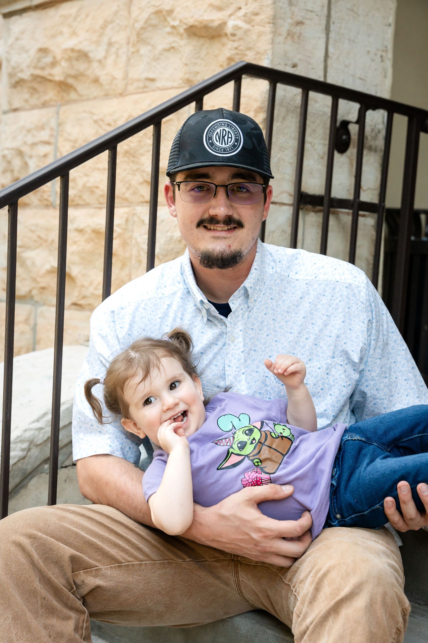 A child in a purple Baby Yoda t-shirt sits on steps with an adult wearing a baseball cap.