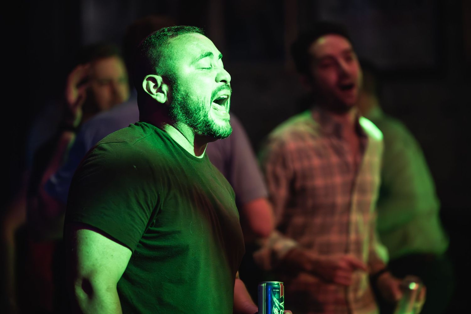 Concert attendee singing along enthusiastically under green stage lighting at live music show.