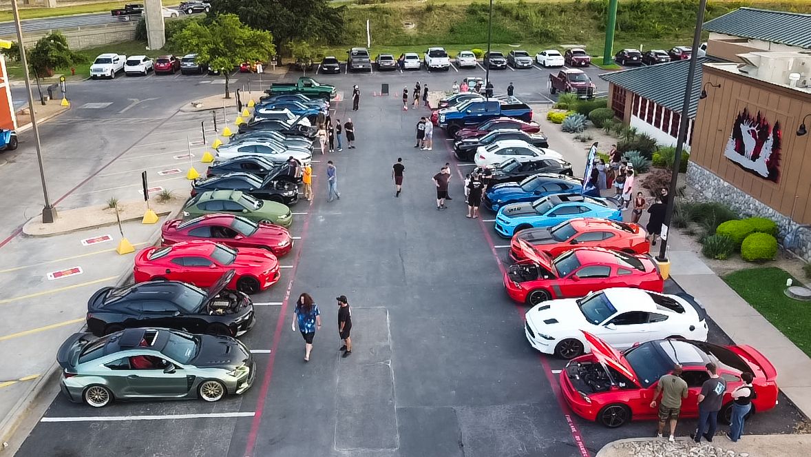 Overhead shot of car show displaying rows of colorful sports cars with spectators walking between.