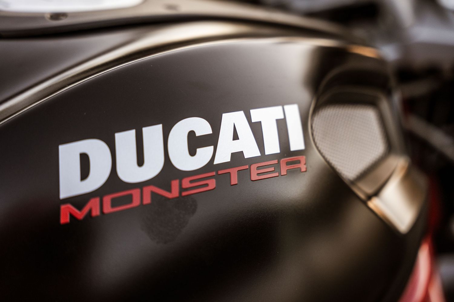 Close-up of Ducati Monster motorcycle logo on black fuel tank.