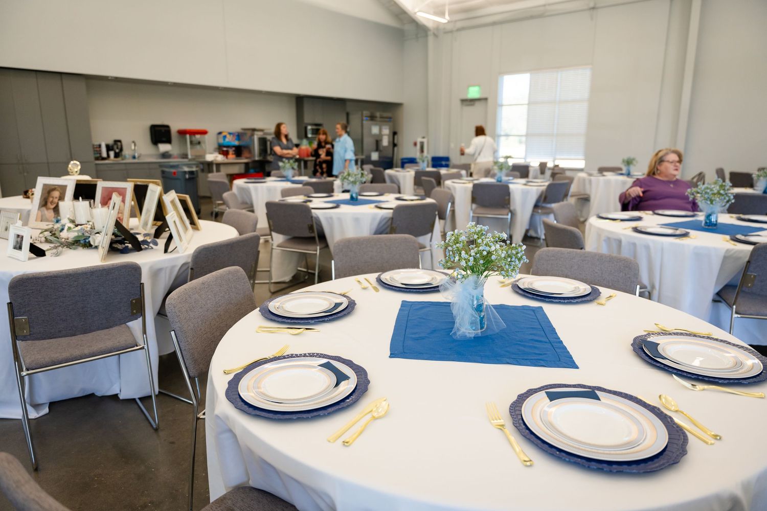 Reception hall with round tables set with blue placemats and white plates.