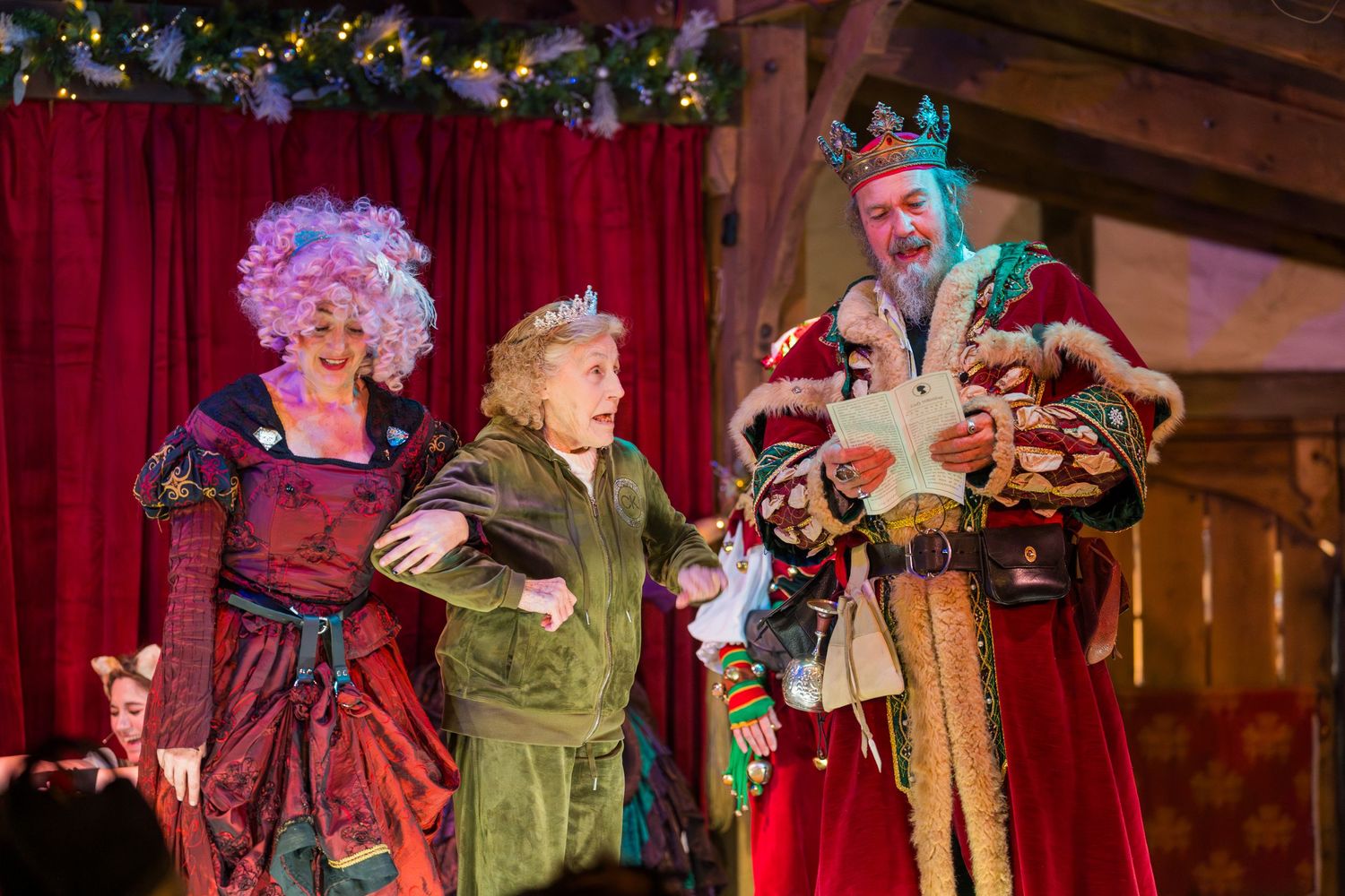 Medieval theater performers in elaborate costumes acting on a decorated holiday stage.