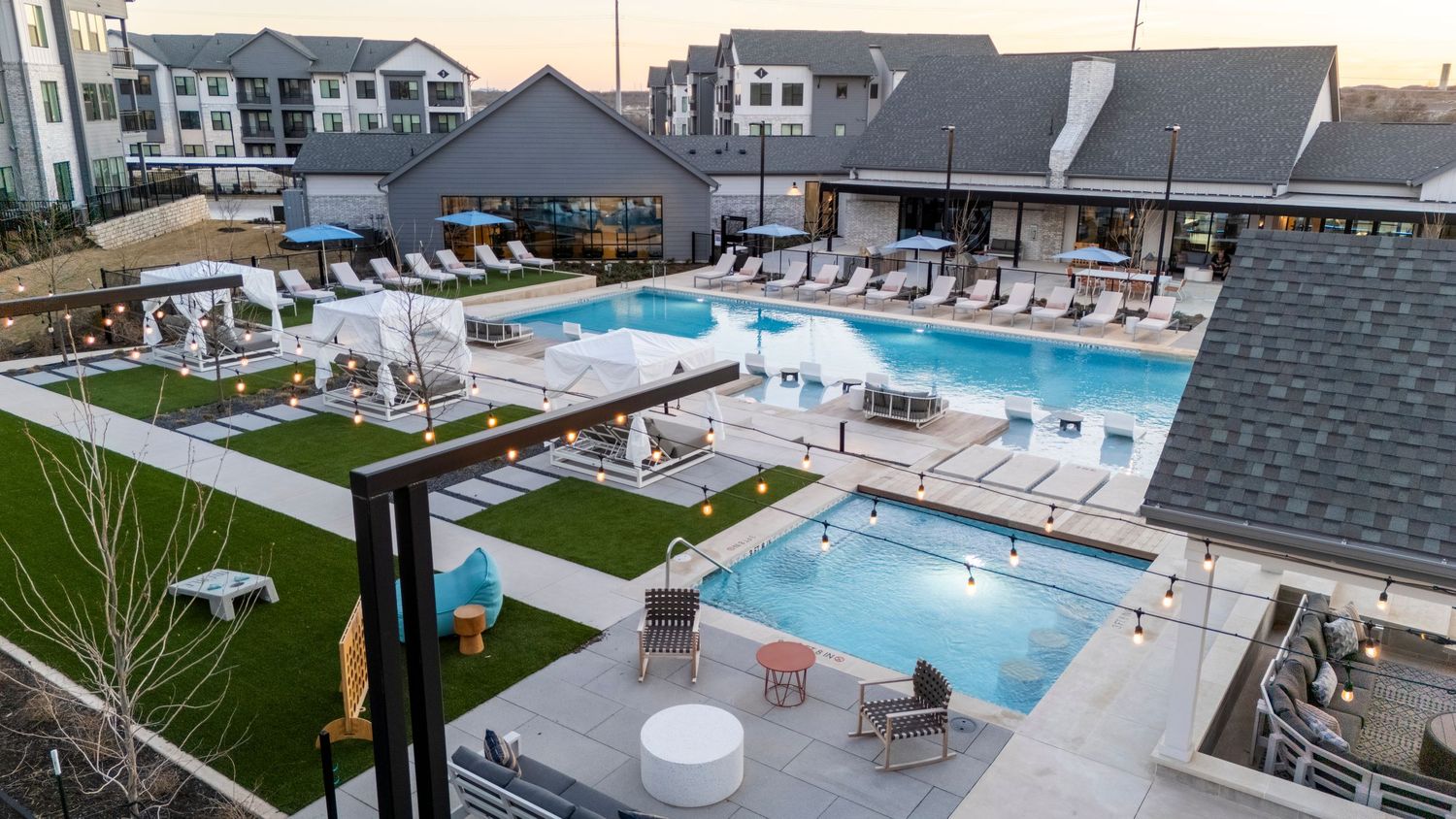 Elevated view of a luxury residential complex featuring multiple swimming pools and outdoor lounging areas at sunset.