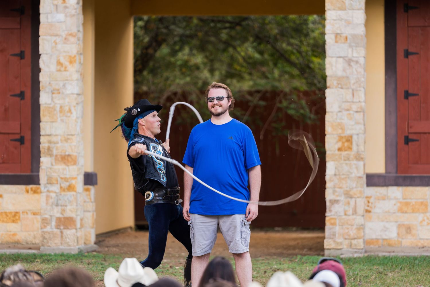 A whip demonstration performance in front of a stone building at a Renaissance festival.