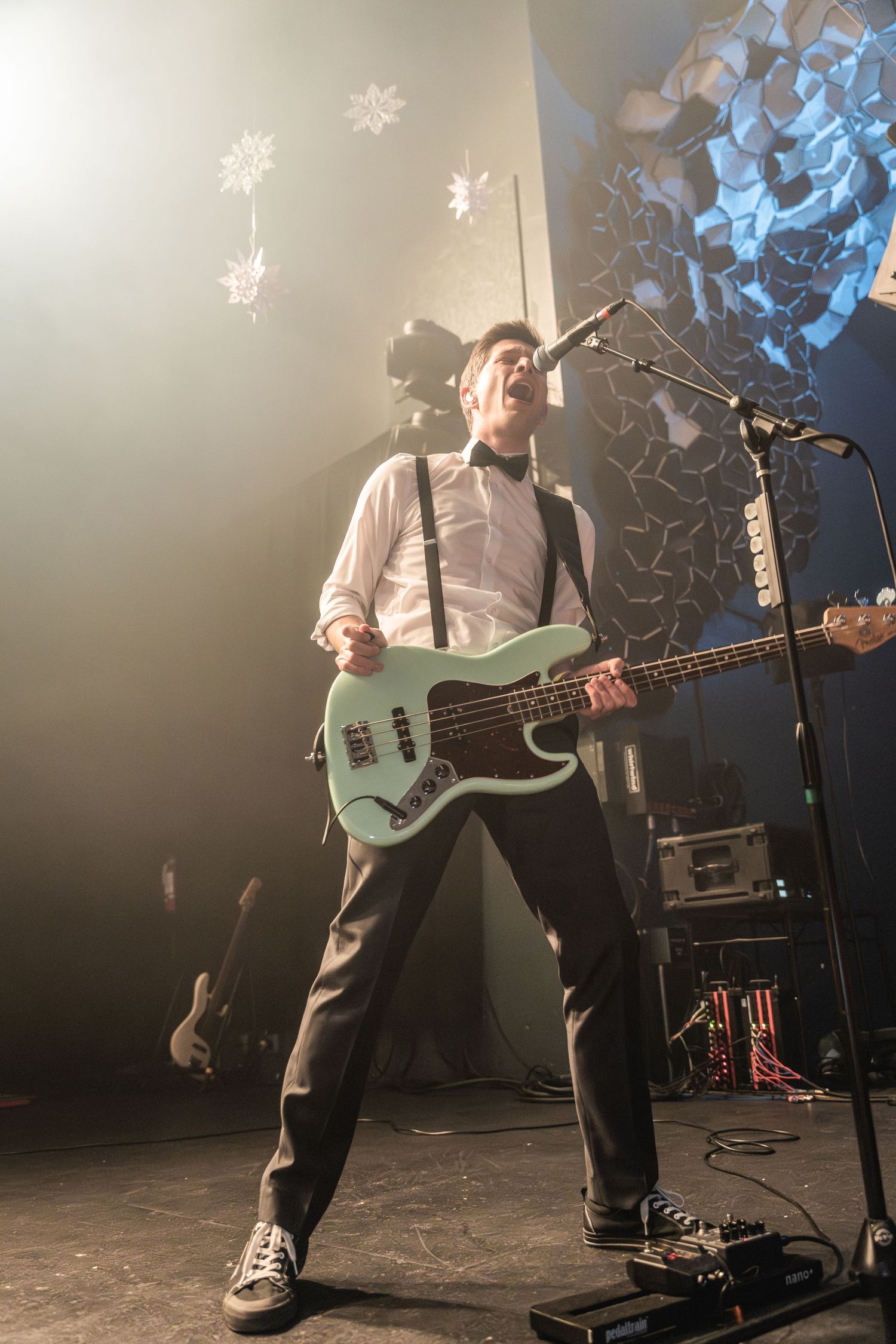 Musician plays bass guitar on stage with decorative snowflakes in the background.