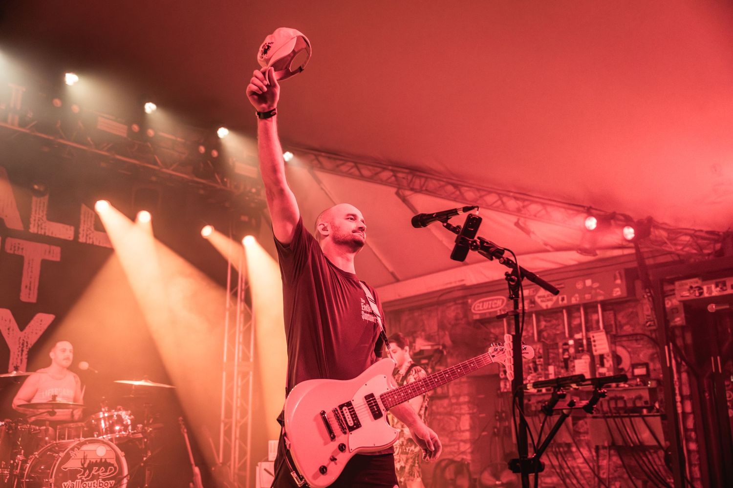 Musician performs on stage bathed in dramatic red lighting while holding guitar overhead.
