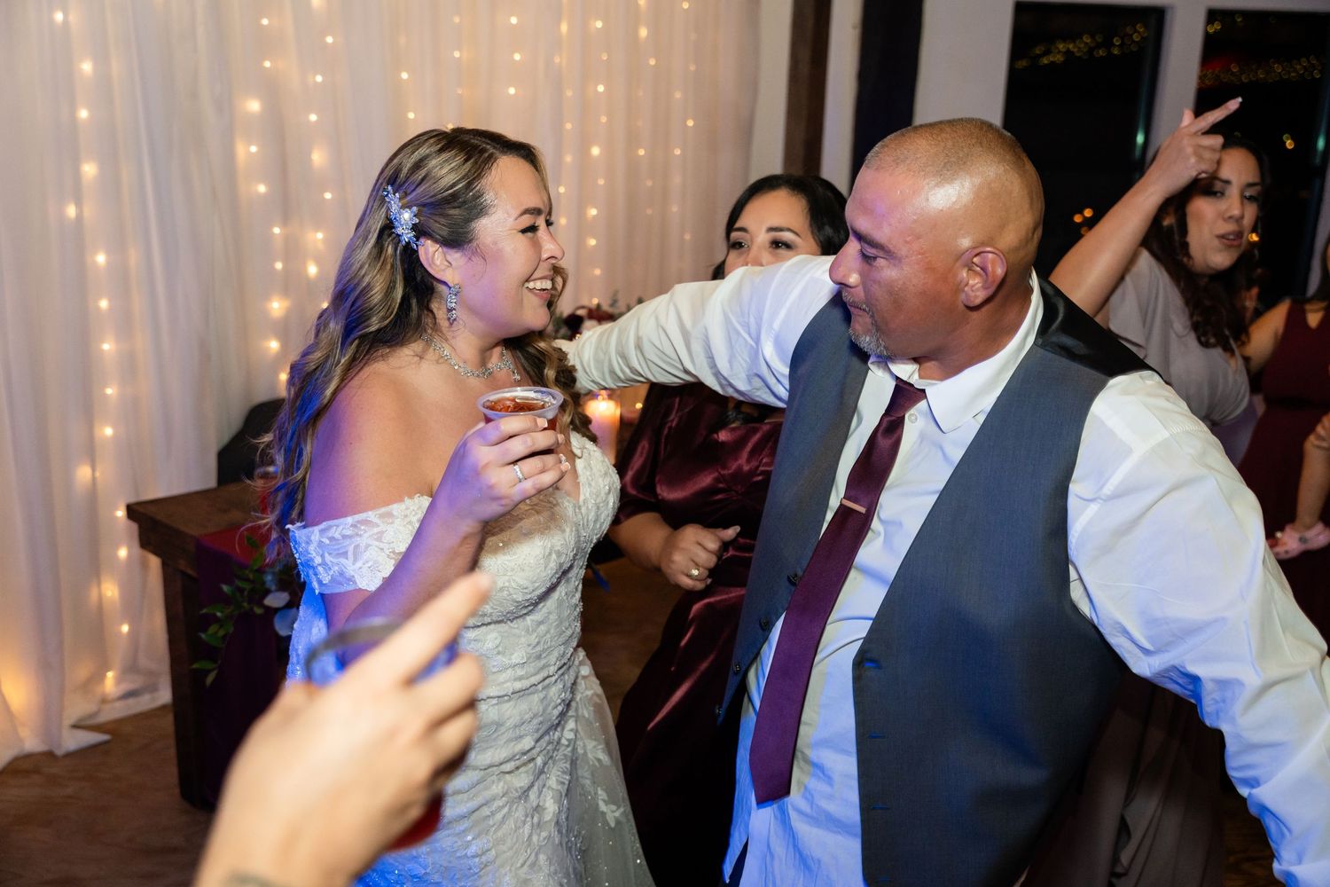 Wedding celebration reaches peak excitement as guests celebrate on the dance floor with string lights behind.
