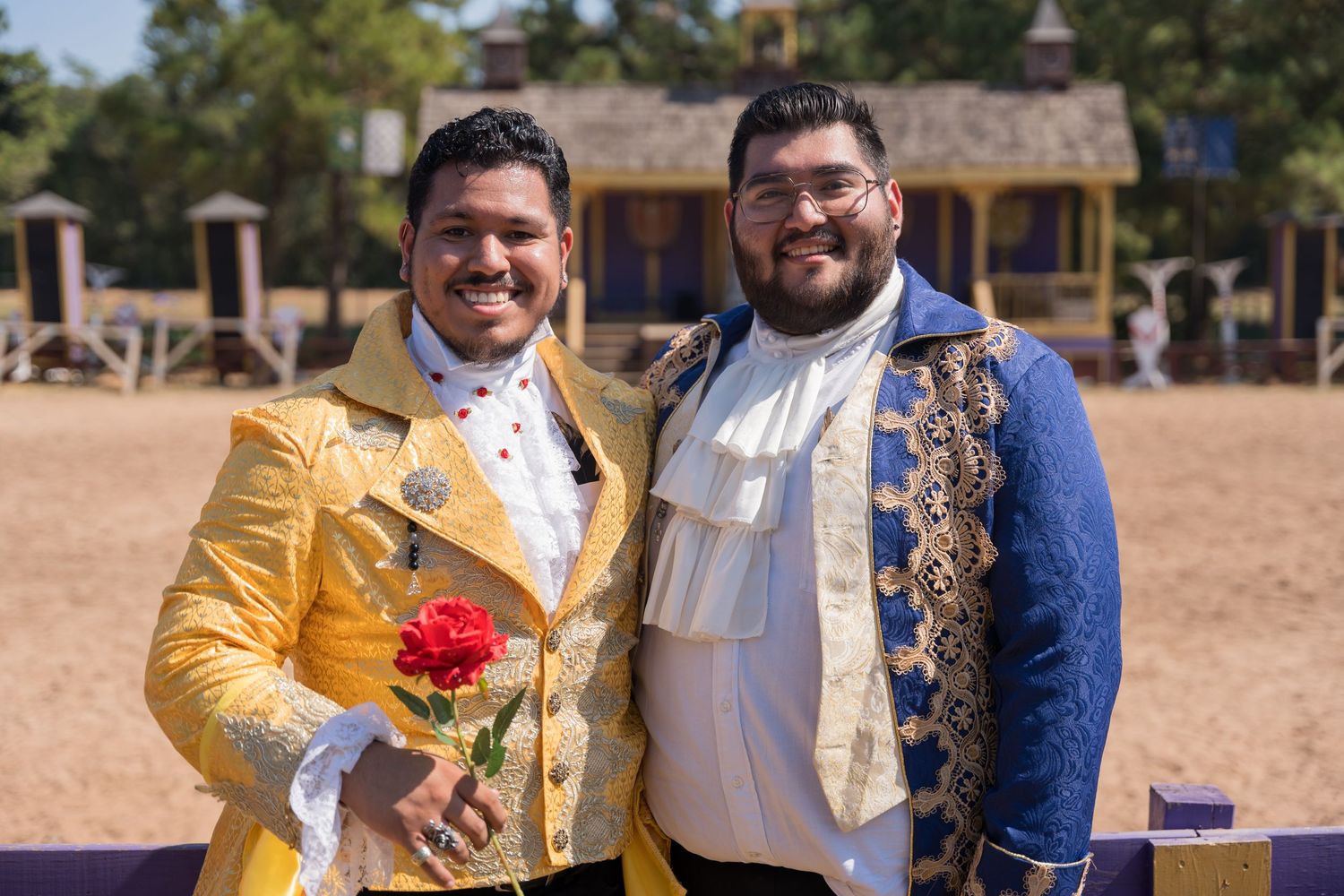 Two performers in ornate period costumes with bright gold and blue jackets pose at a renaissance fair.
