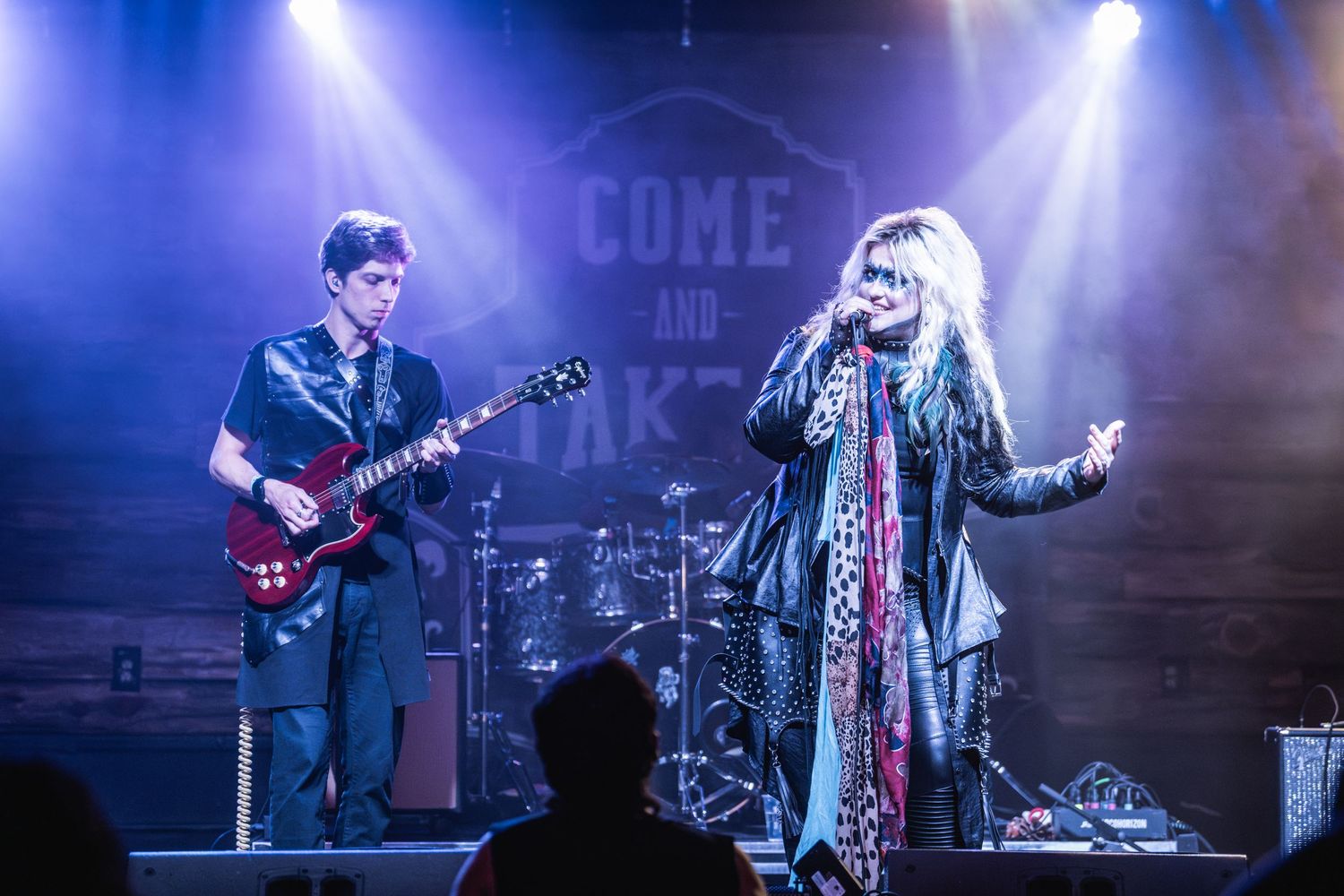 Rock band performing on stage with dramatic lighting and musical instruments.