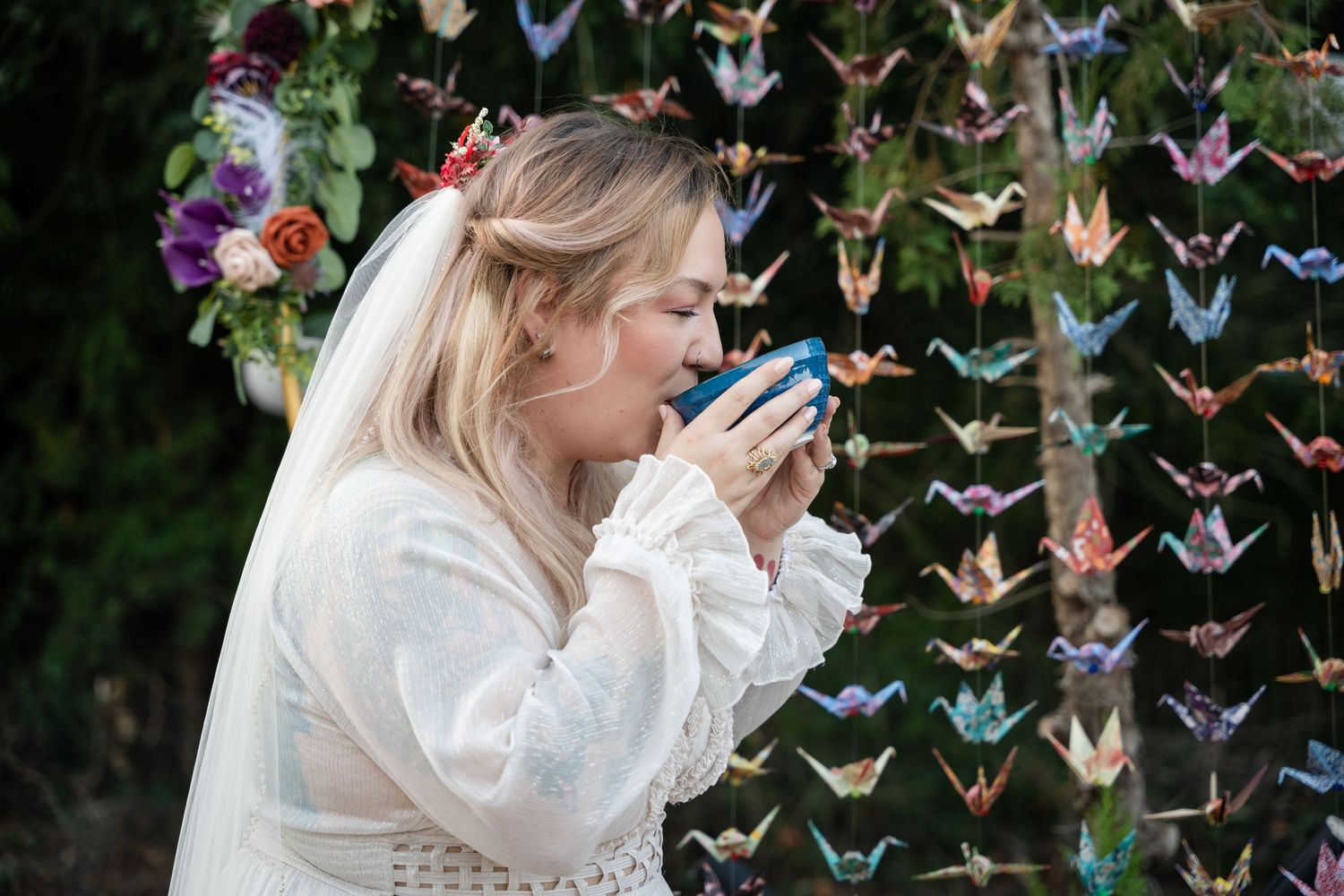 A person in white gazes at colorful origami butterflies hanging in the garden setting.