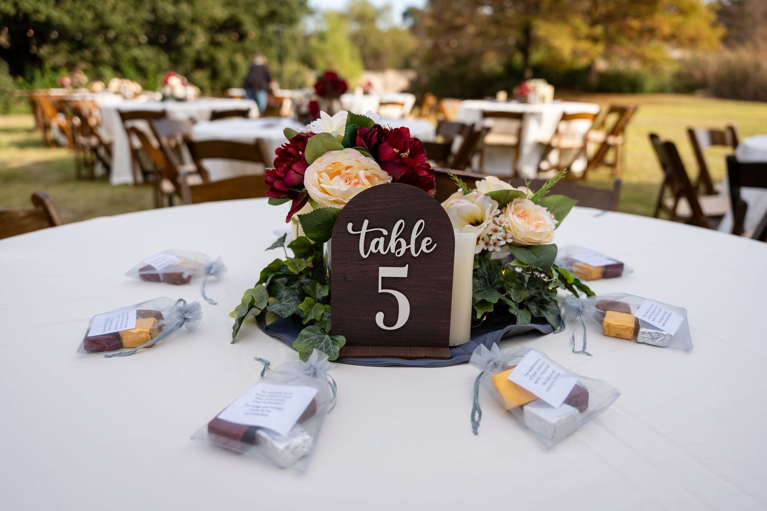Elegant wedding table centerpiece with burgundy flowers and wooden table number 5 sign on white linen.