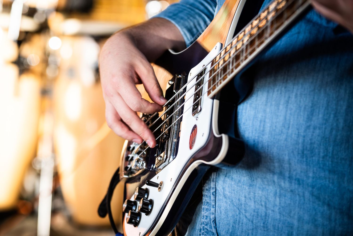 Close-up shot of hands playing electric bass guitar strings against blurred background.