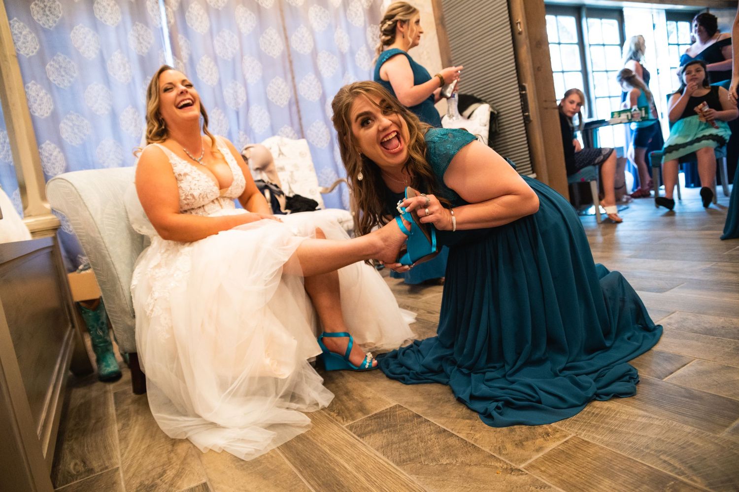 Two people laugh together during wedding preparations in a getting-ready room.
