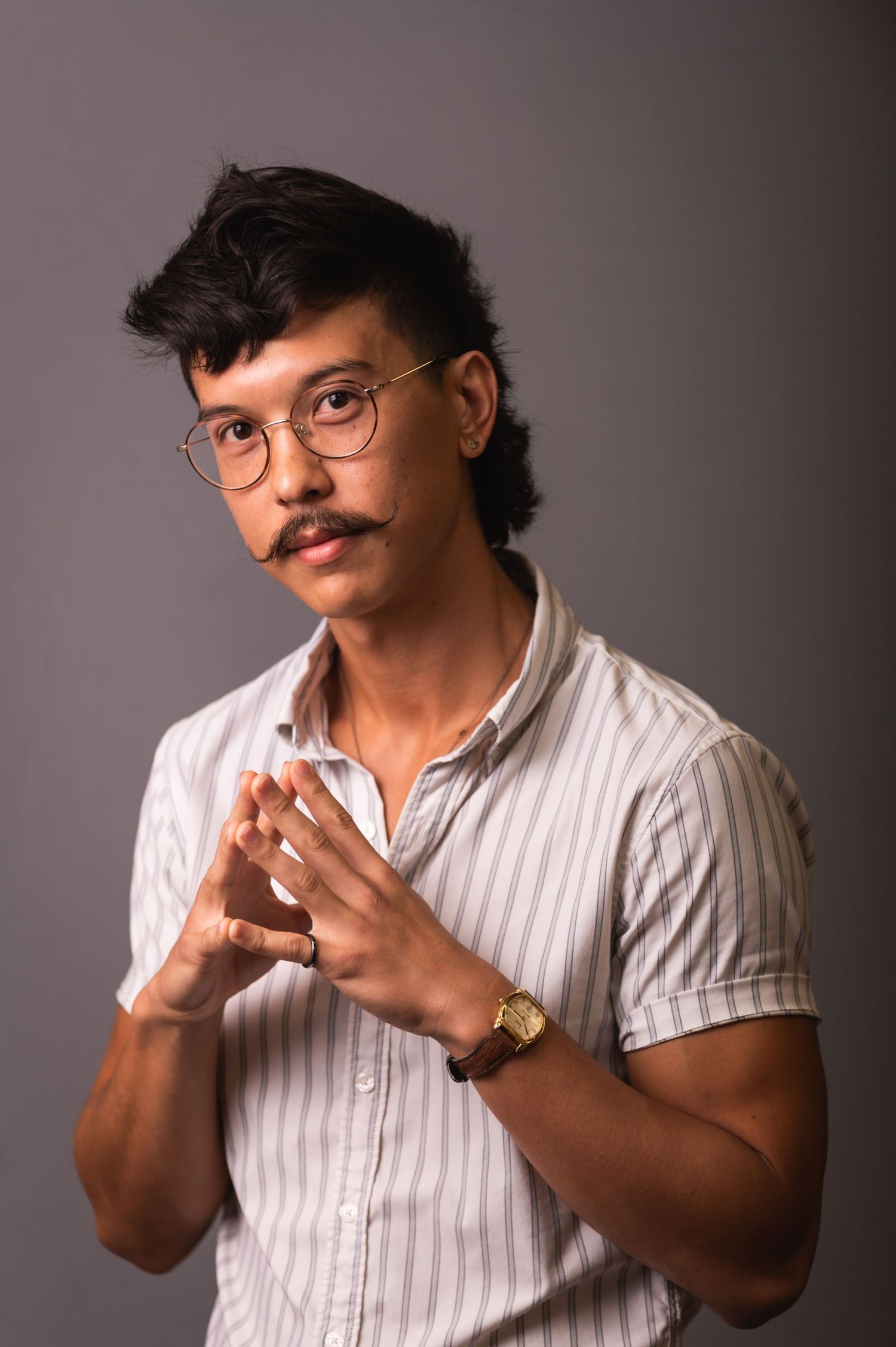 Portrait of person in glasses wearing striped shirt against grey background.