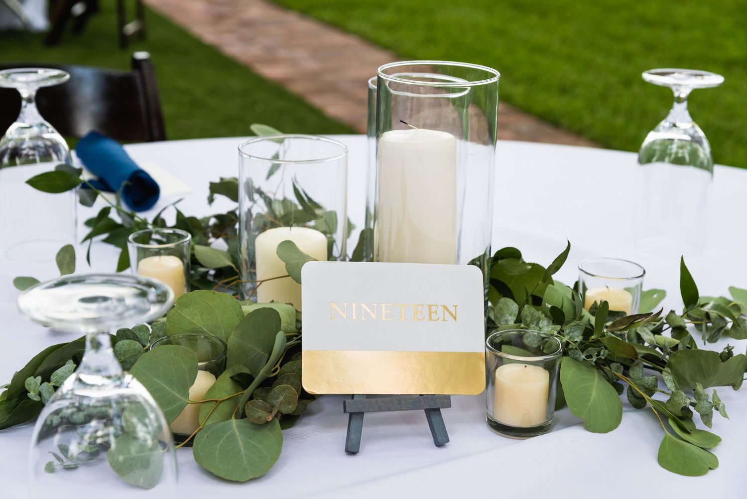 Elegant wedding table setting with eucalyptus garland, candles and gold signage.