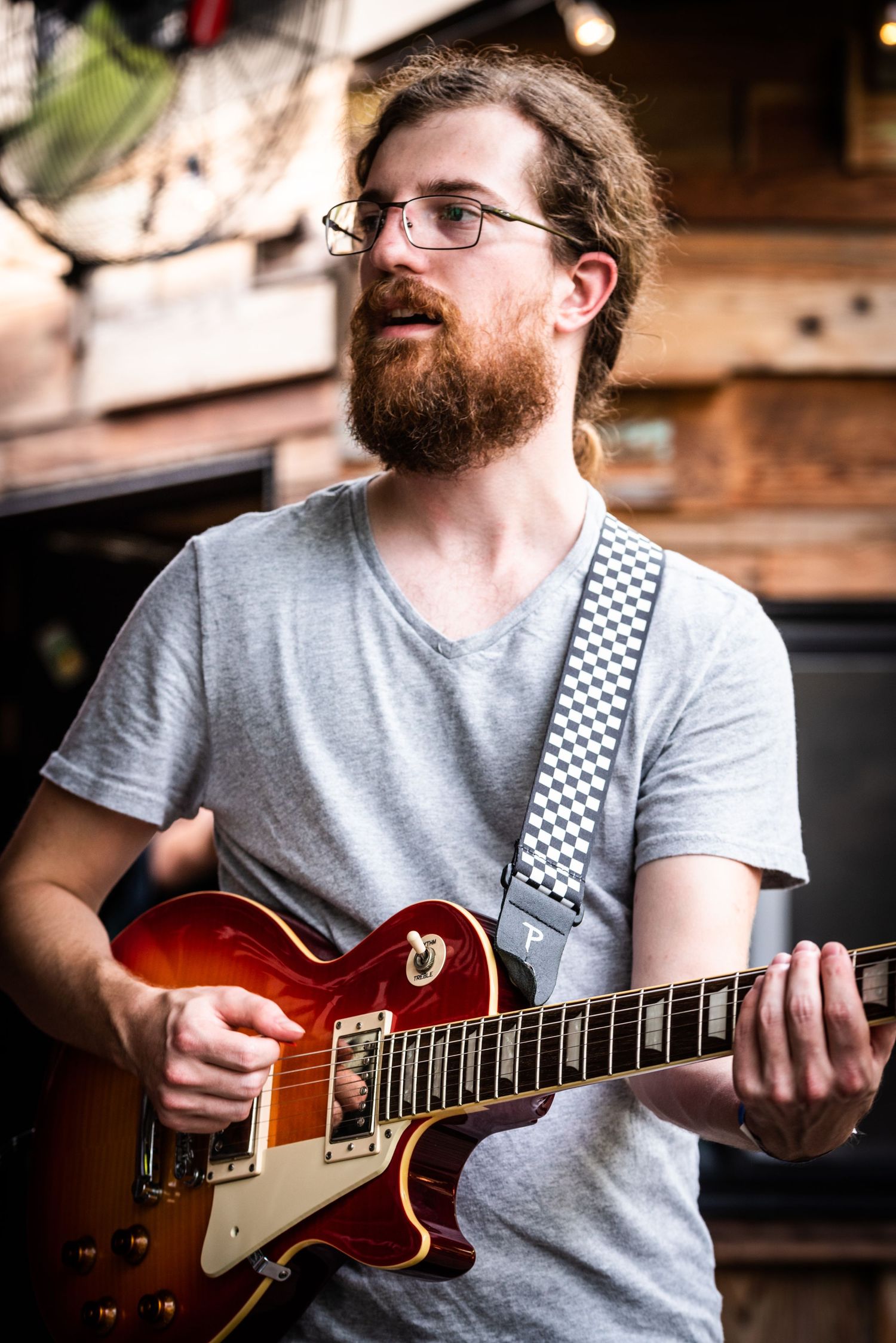 Guitarist with a beard playing a red electric guitar during a live performance.