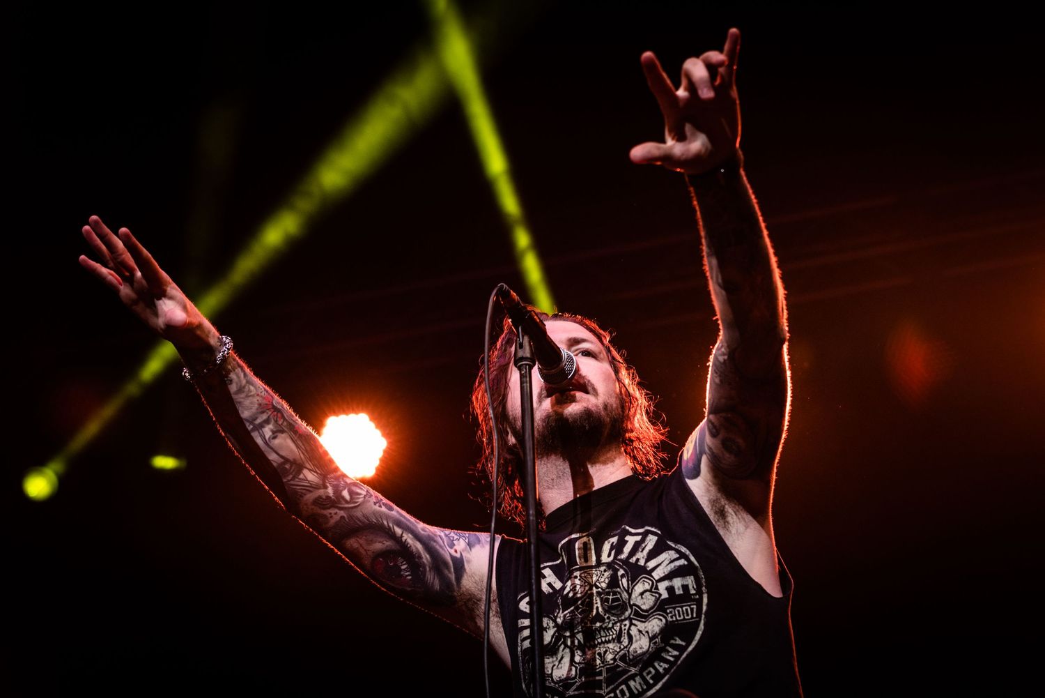 A performer with tattoos raises both arms during an intense concert moment.