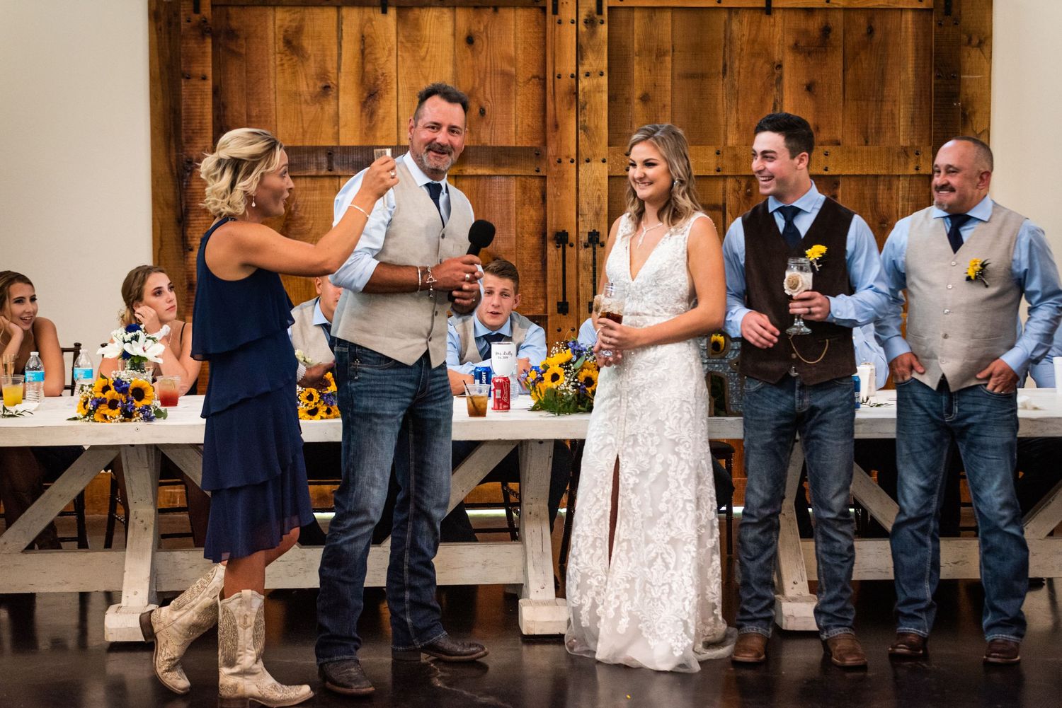 Wedding celebration group shares drinks and laughter during reception in rustic barn venue.