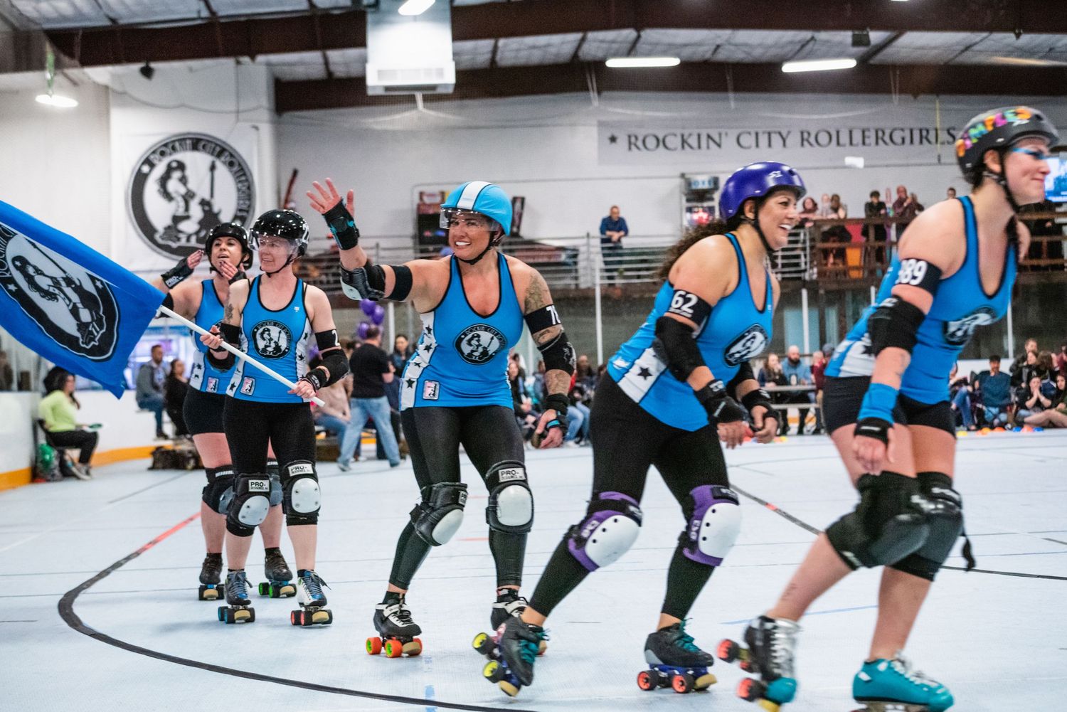 Team of roller derby players in blue uniforms skate together during match.