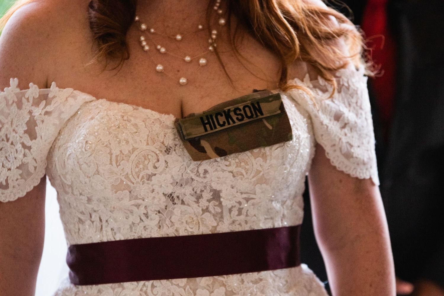Detail shot of lace wedding dress with burgundy sash and pearl necklace.