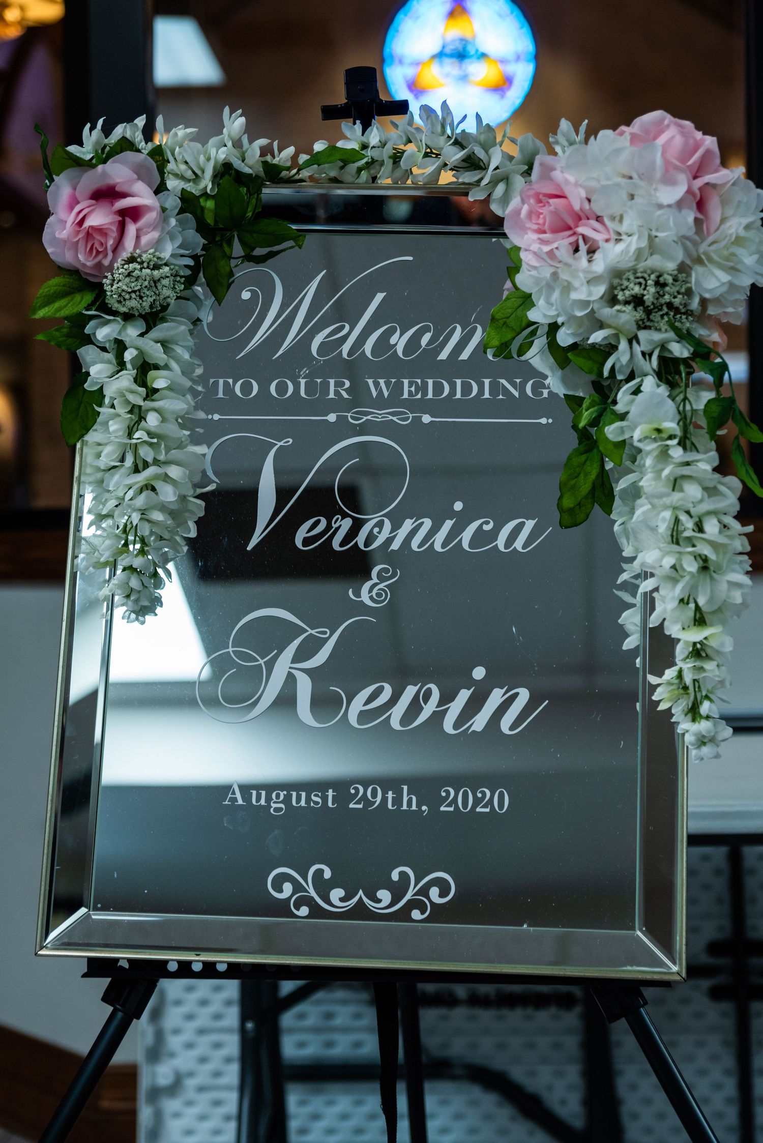Mirrored welcome sign with floral decor announces Veronica and Kevin's wedding date.