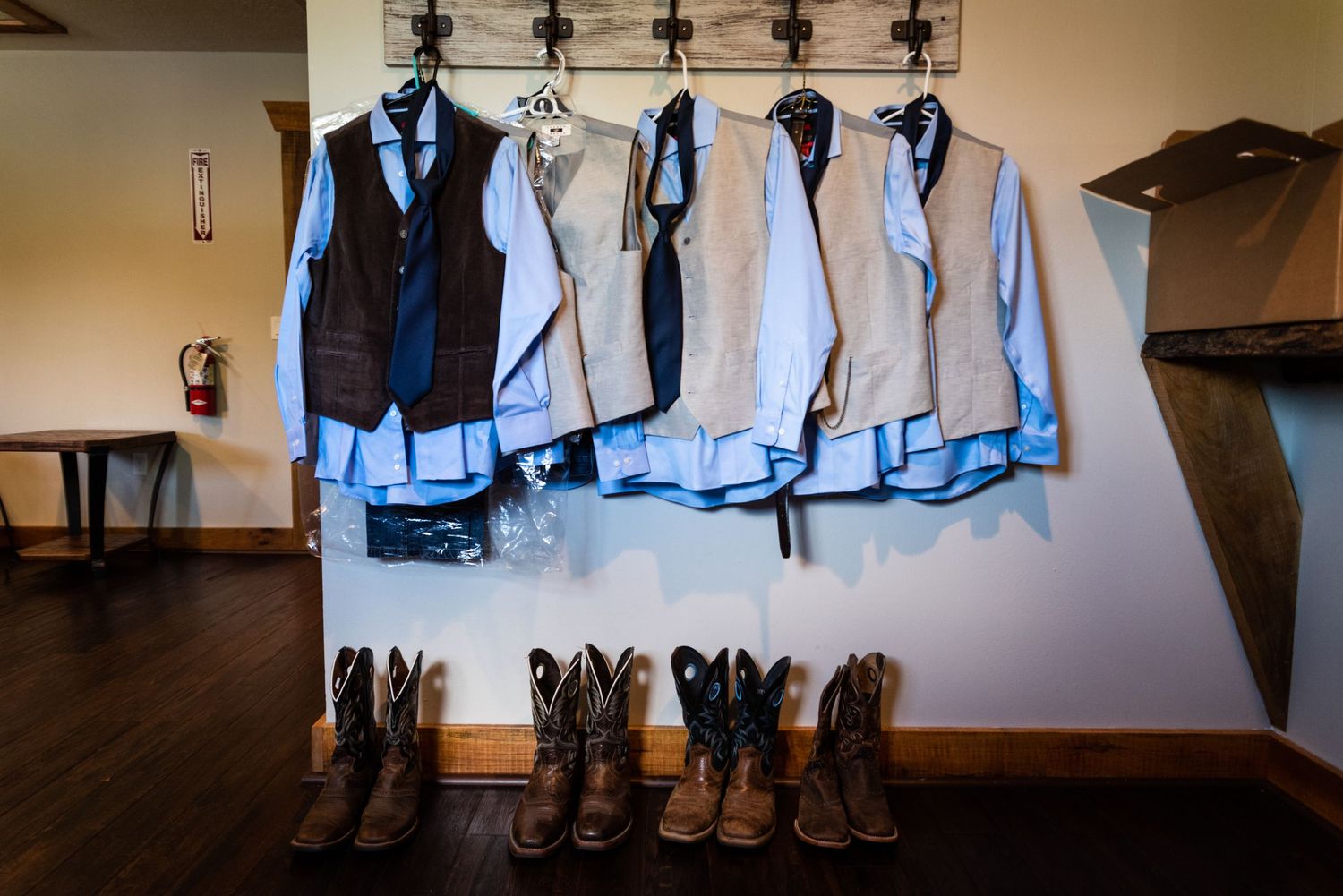 Groomsmen's shirts and vests hanging above a row of cowboy boots.