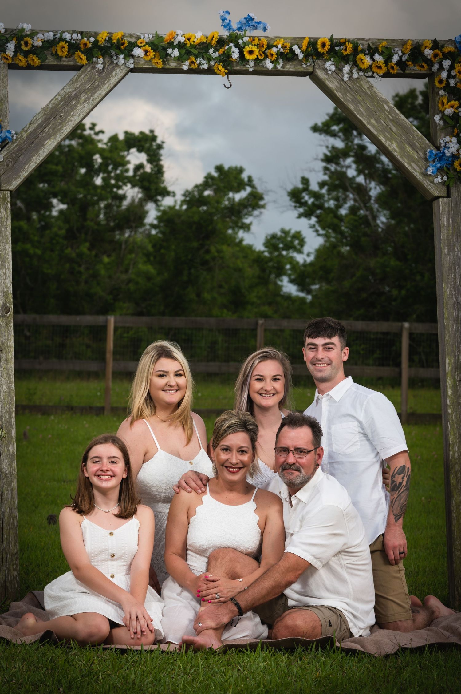 Family group photo under a decorated wooden arch in a backyard setting.