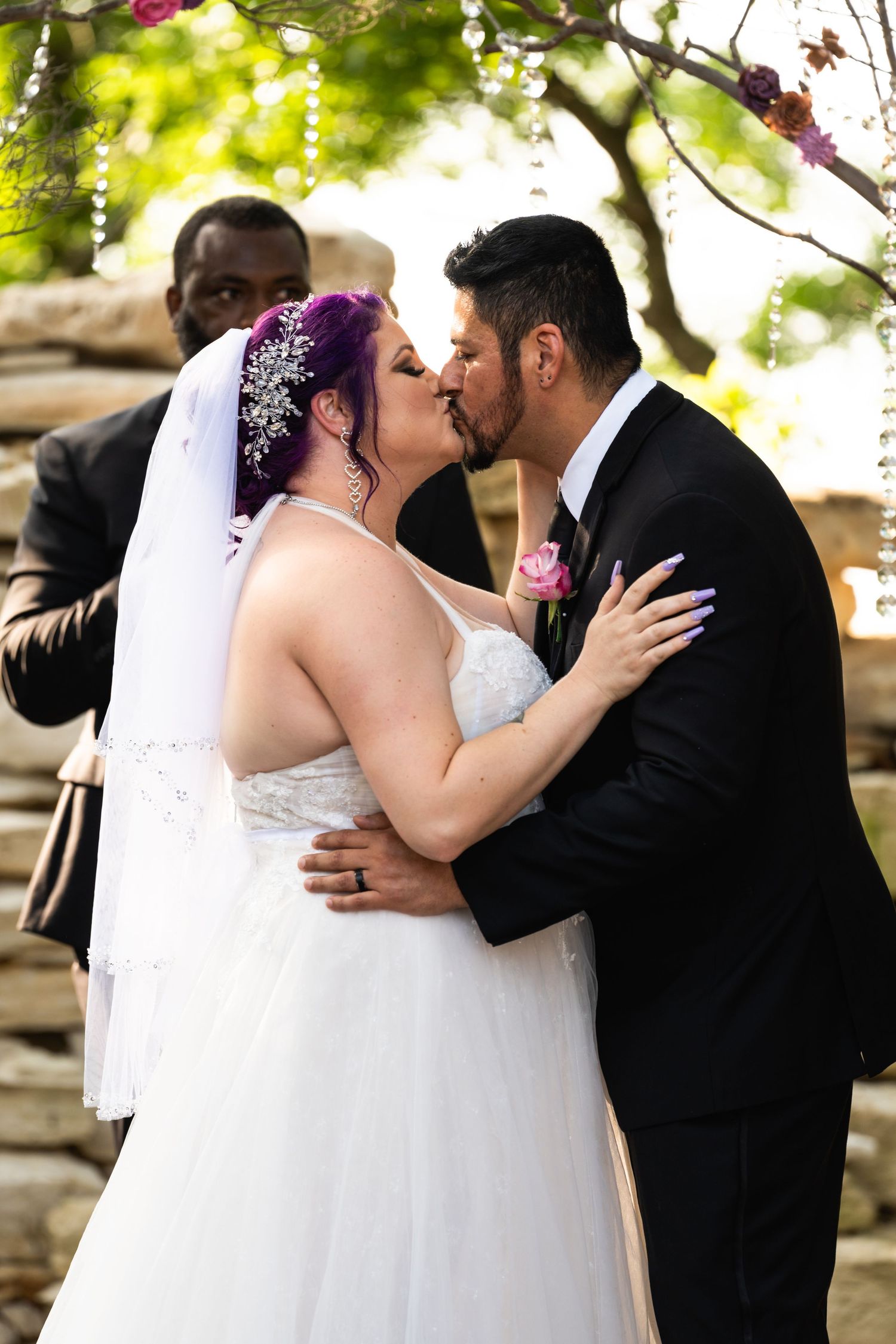 Newlyweds share an intimate kiss against a natural stone wall backdrop at their outdoor wedding.