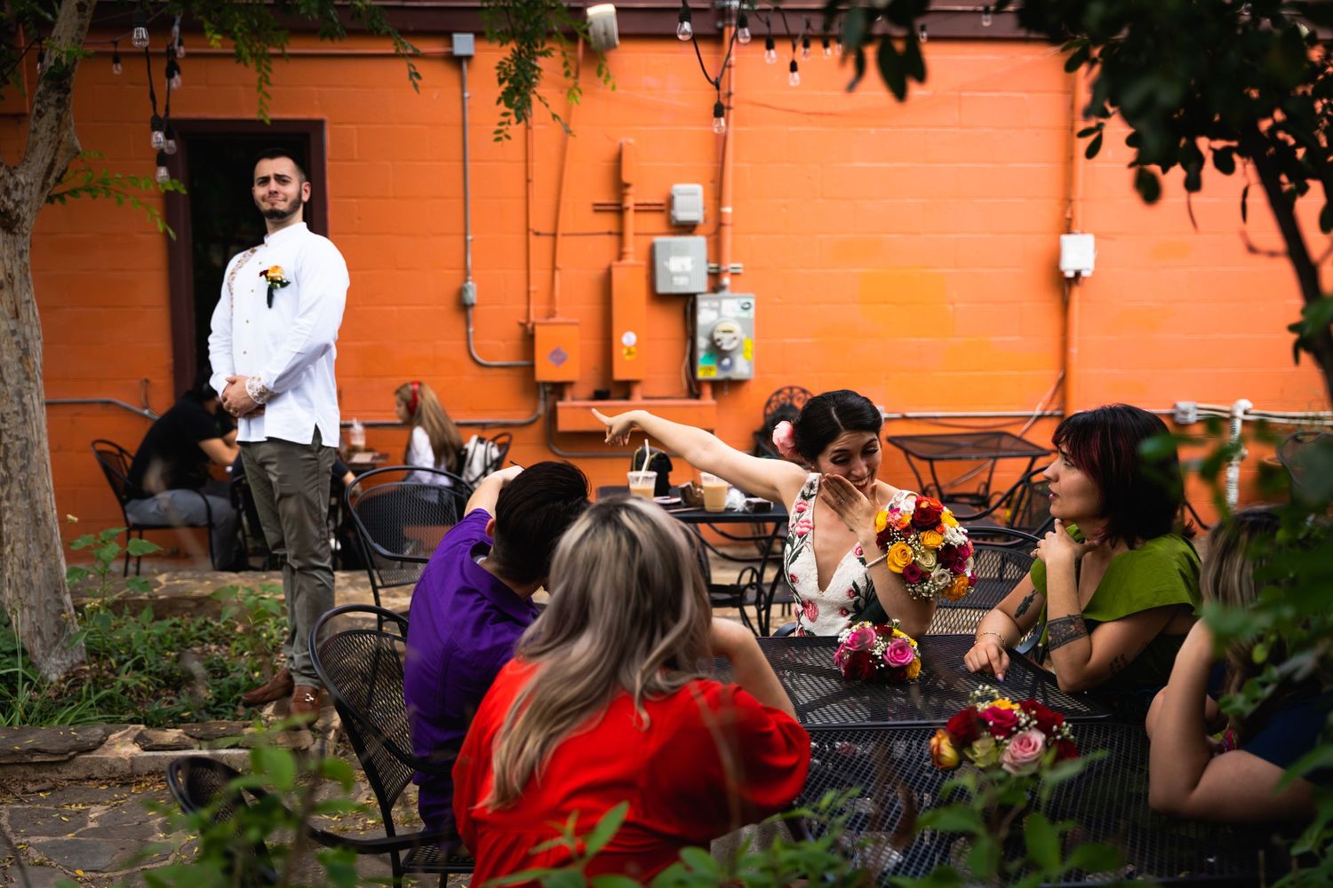 Wedding guests enjoying an outdoor reception with orange wall backdrop.