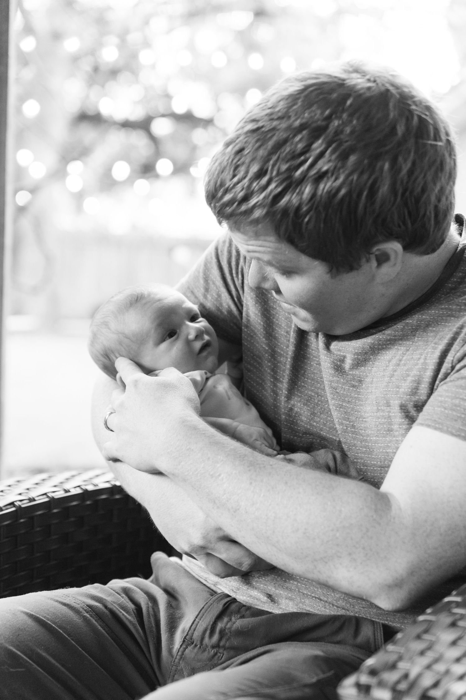 An intimate black and white portrait of a newborn being held on outdoor patio furniture.