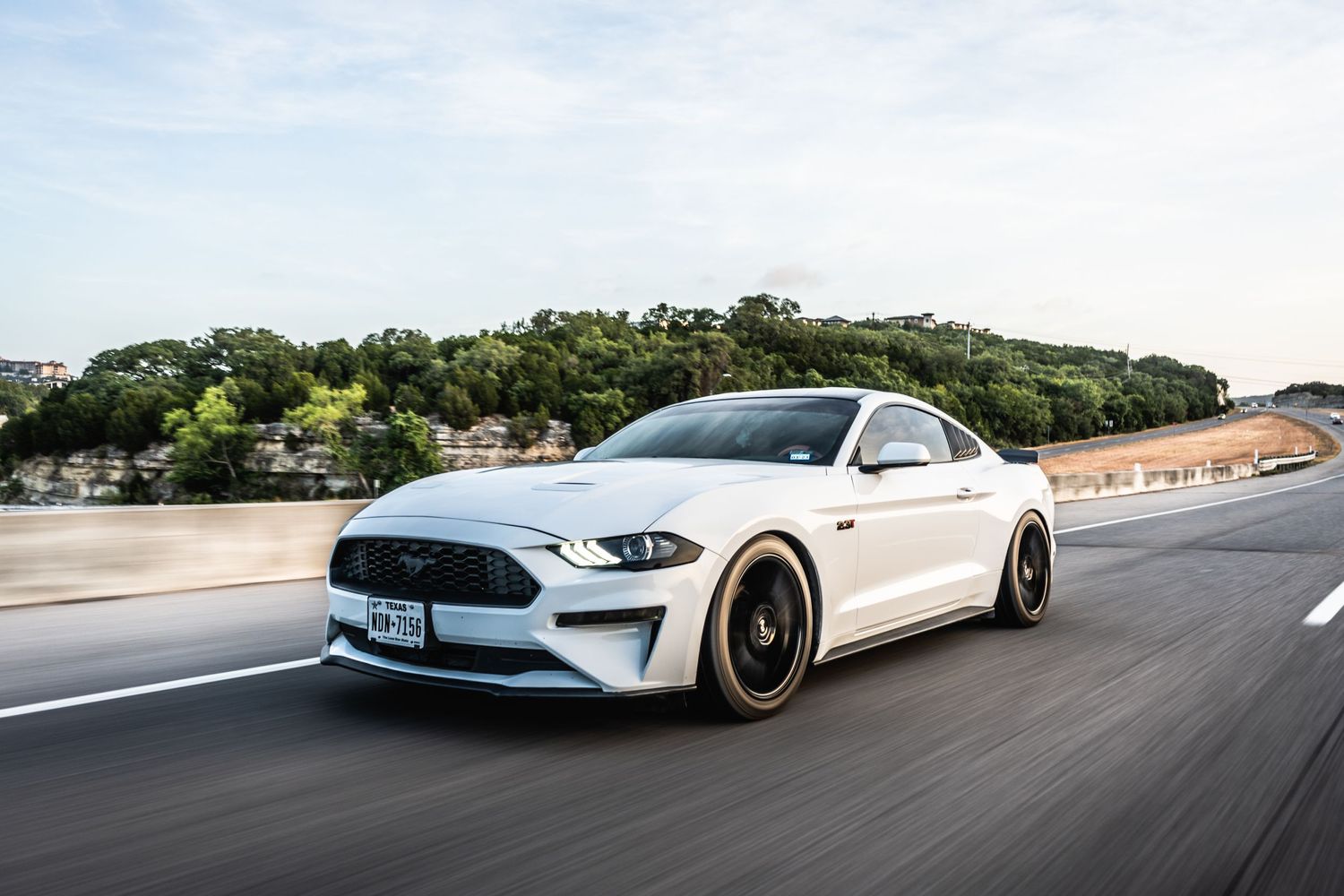 Ford Mustang in pearl white with custom black wheels cruising on a scenic mountain road.