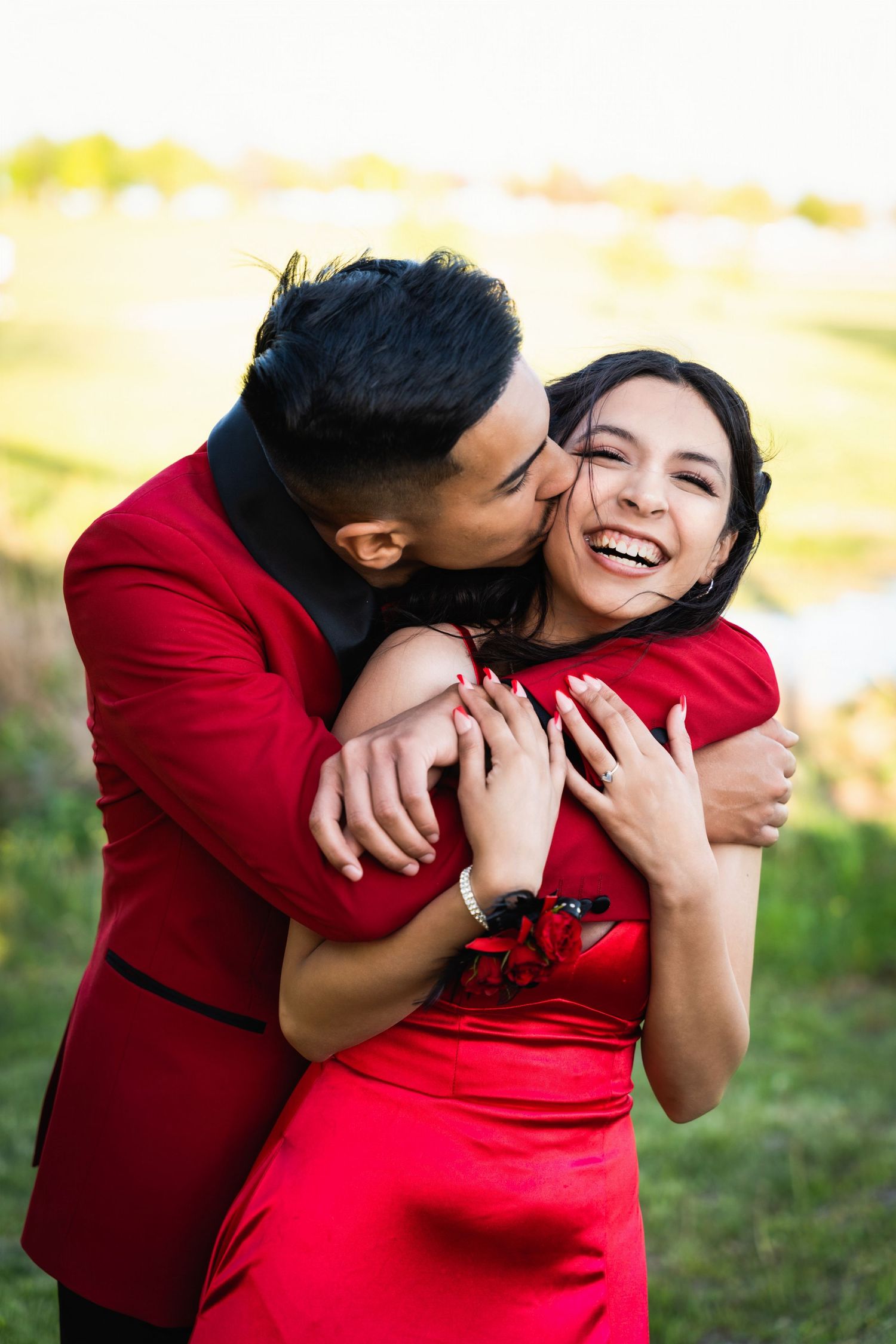Couple in matching red outfits share an intimate embrace while laughing outdoors.