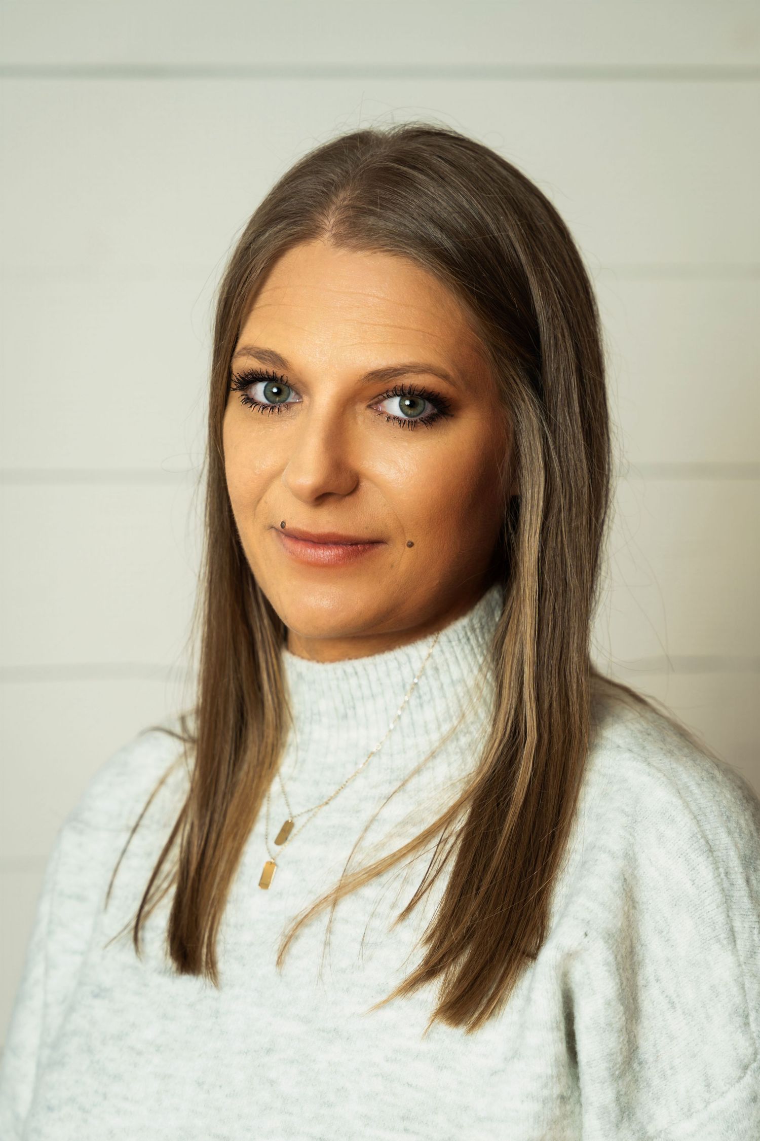 Professional portrait of person in white sweater with cross necklace against light background.