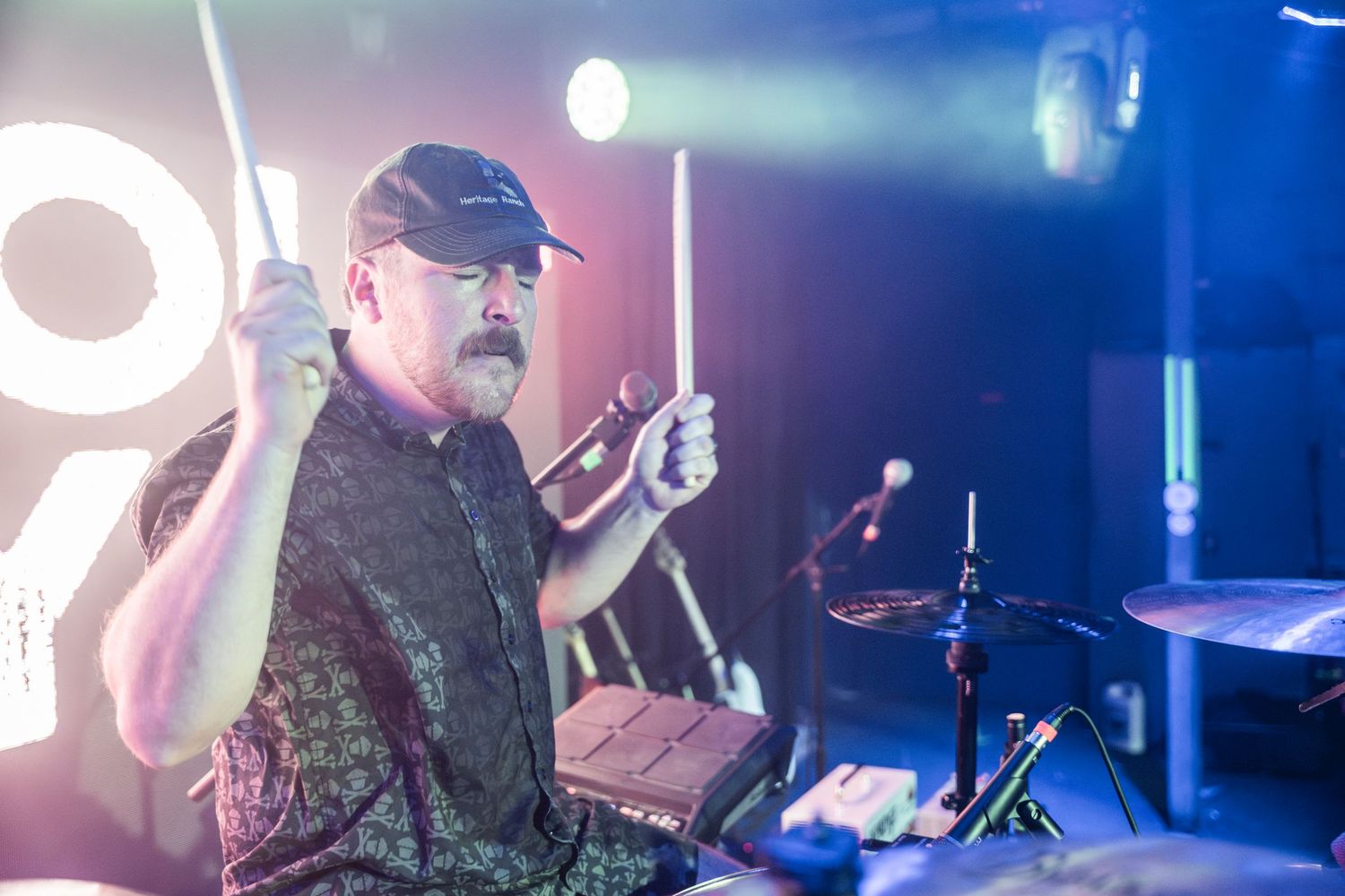 A concert stage setup with blue lighting and a drummer performing during a live music show.